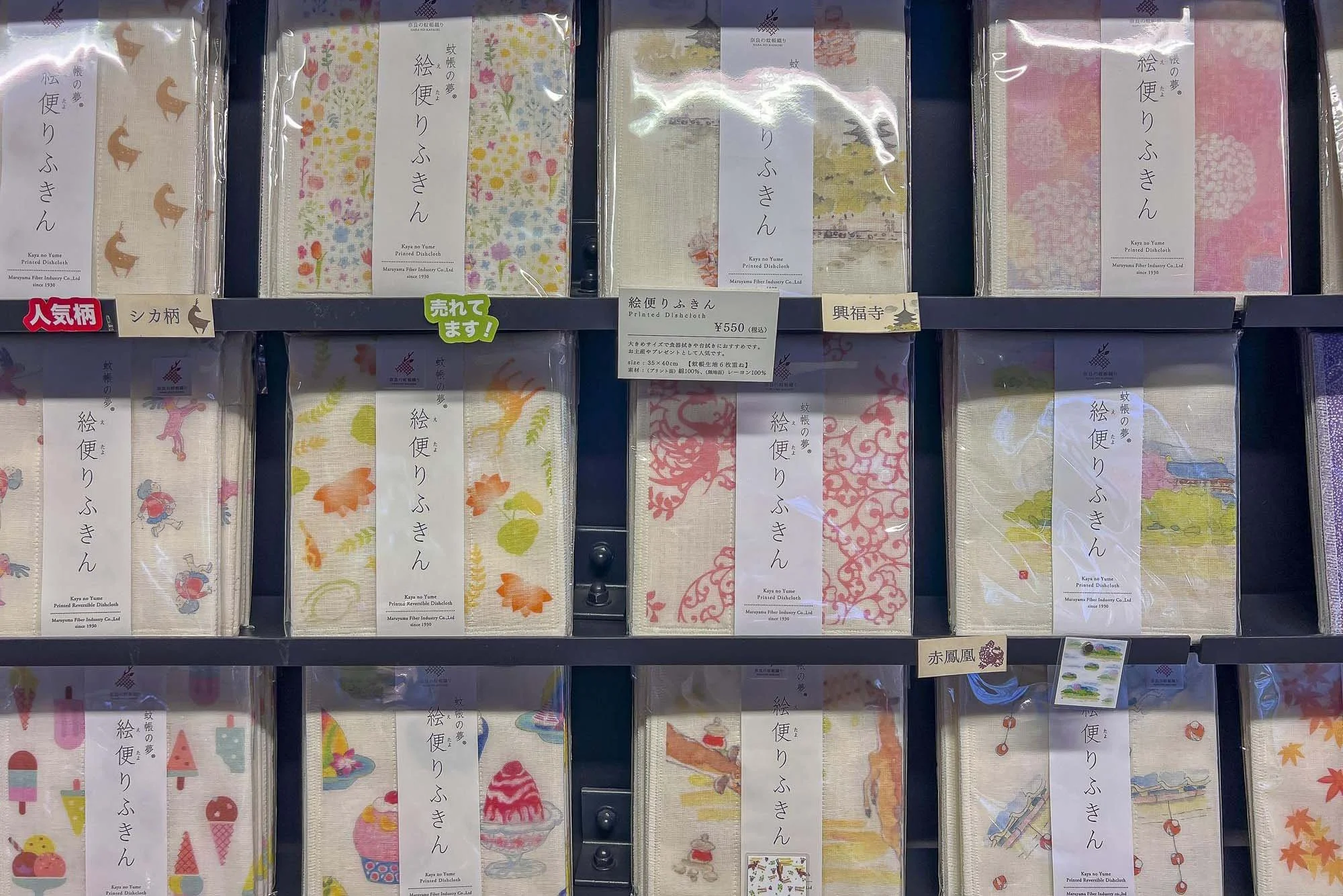 Display of various colorful Japanese printed handkerchiefs hanging on a store shelf, each with different patterns including animals, flowers, and traditional motifs.