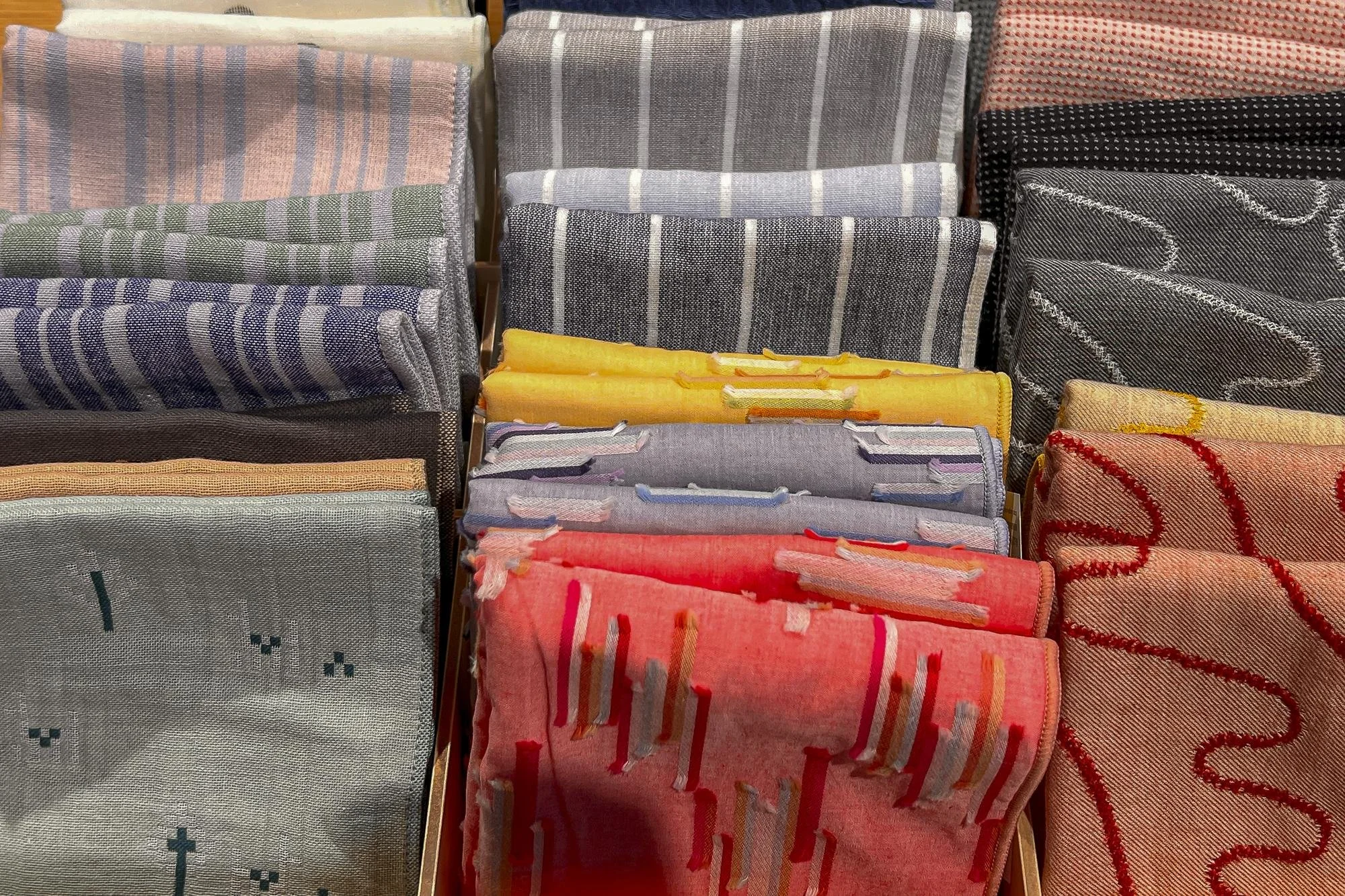 Stacked folded fabric napkins or towels in various colors and patterns, arranged upright in display trays.