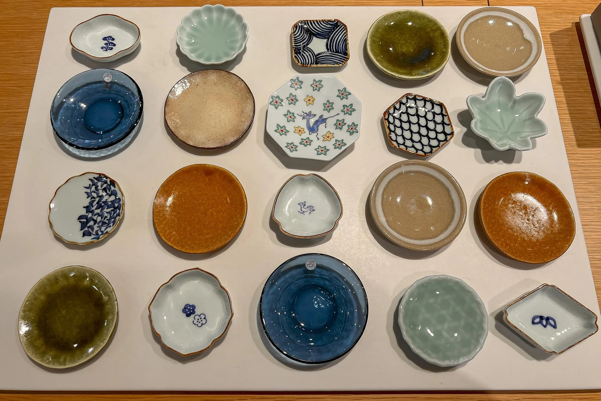 A display of various small, colorful ceramic bowls arranged on a white surface, with wood table edges visible.
