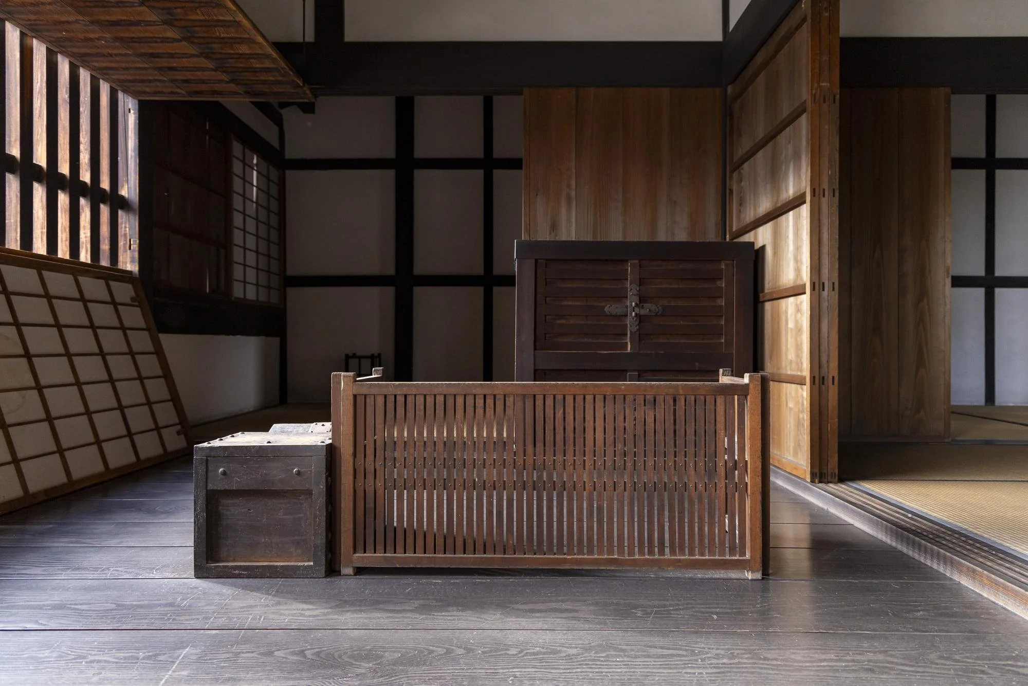 Interior of a traditional Japanese room featuring wooden walls, sliding shoji screens, and wooden furniture, with sunlight filtering through the windows.