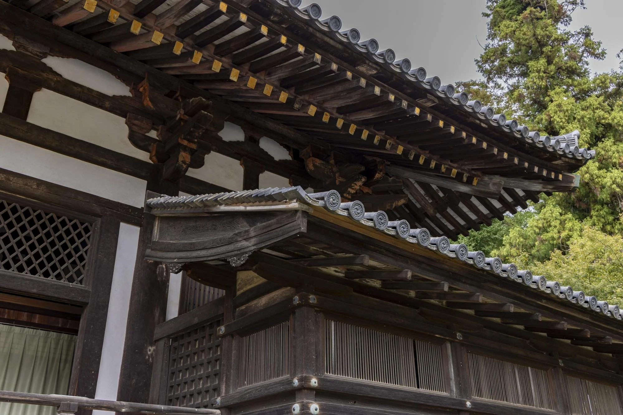 Close-up of traditional Japanese wooden temple roof with ornate tile details and green trees in the background.