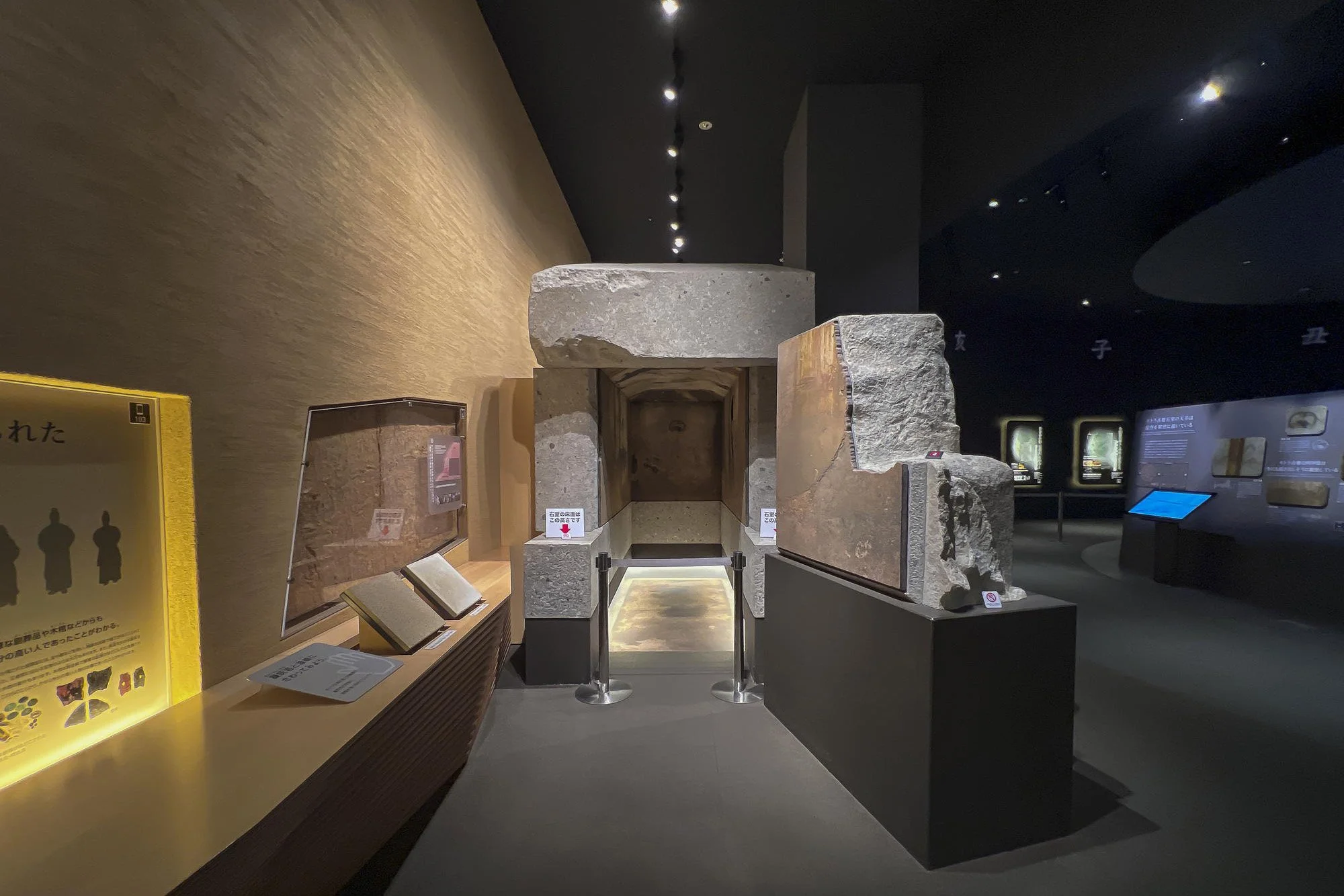 Ancient stone artifacts displayed in a museum exhibit, with informational signage on the left and a dark background with more displays on the right.