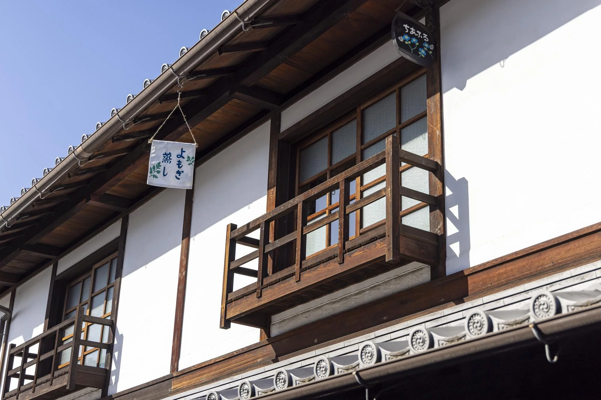 Image of a traditional Japanese building with wooden balconies, white walls, tiled roof, and hanging signs with Japanese characters.