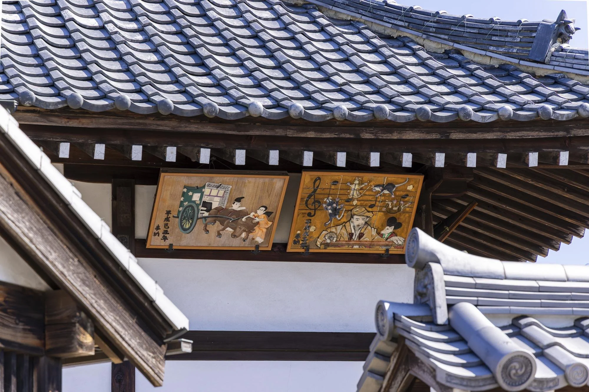 Decorative wooden plaques with Japanese artwork and calligraphy hanging under a traditional Japanese tiled roof.