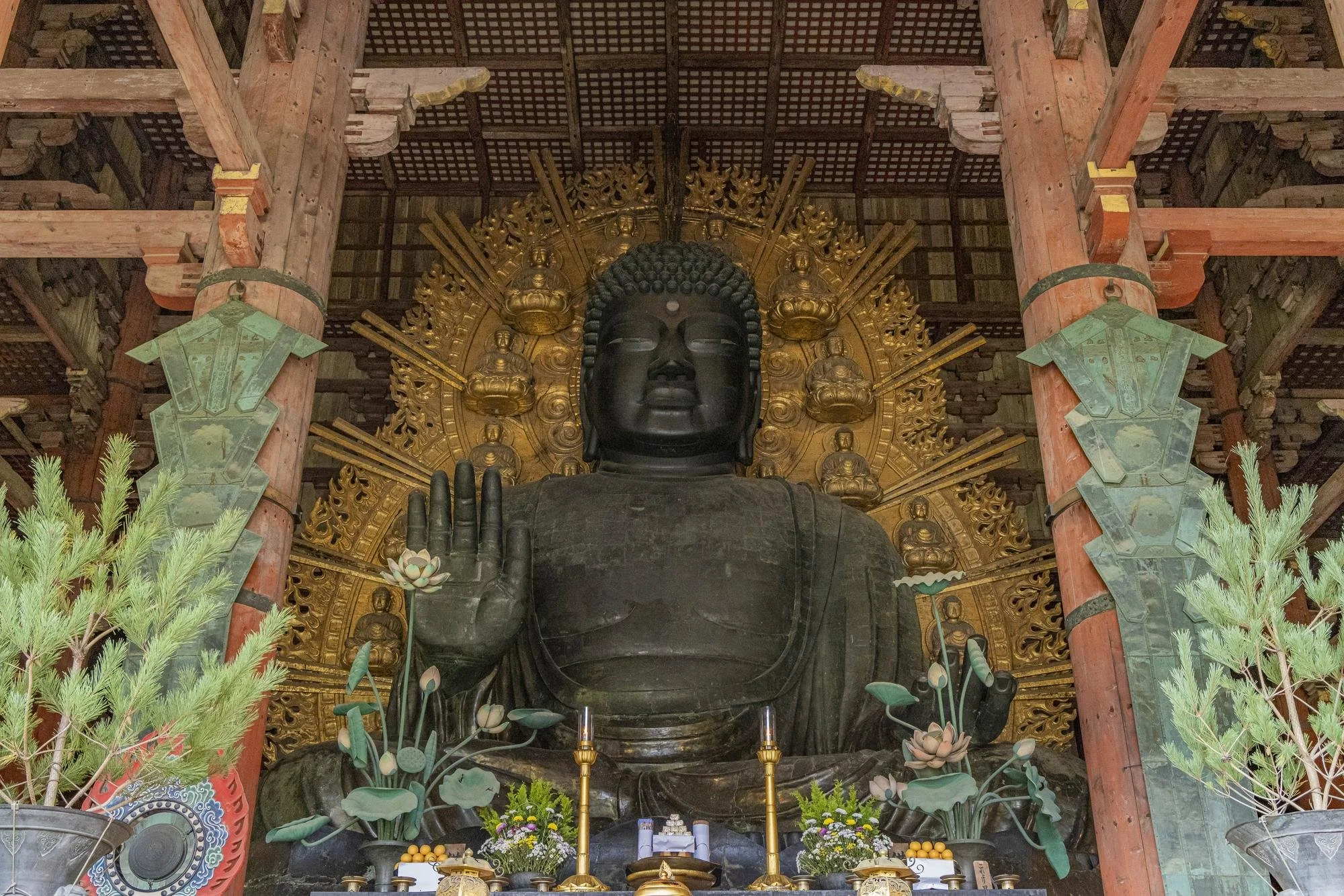 A large traditional Japanese temple with multiple tiers and ornate roofing, surrounded by visitors, under a partly cloudy blue sky