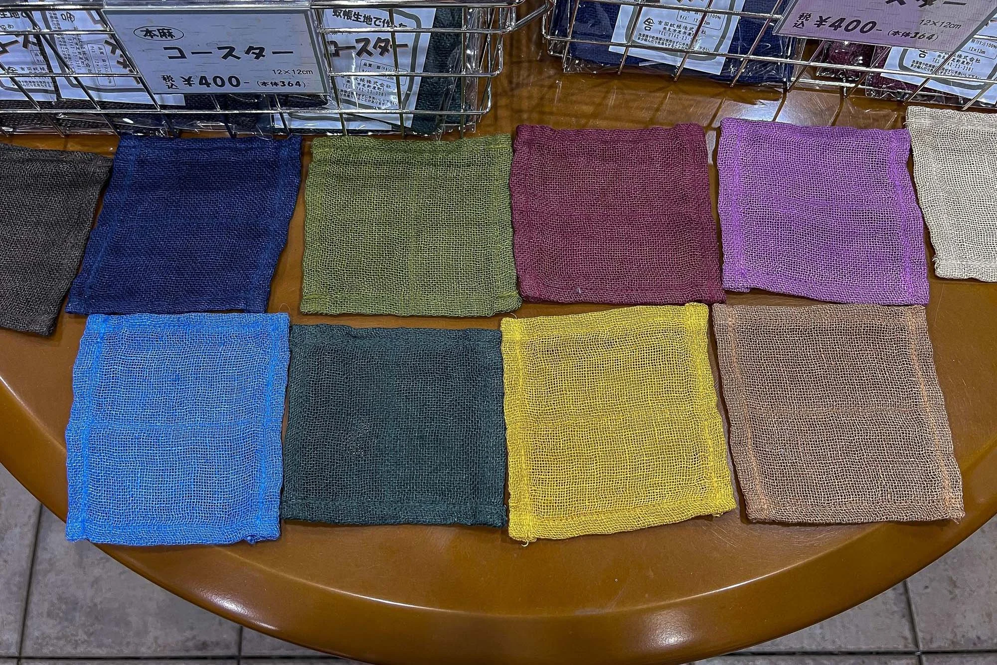 Colorful mesh scrubbers arranged on a wooden table with Japanese price tags in the background.