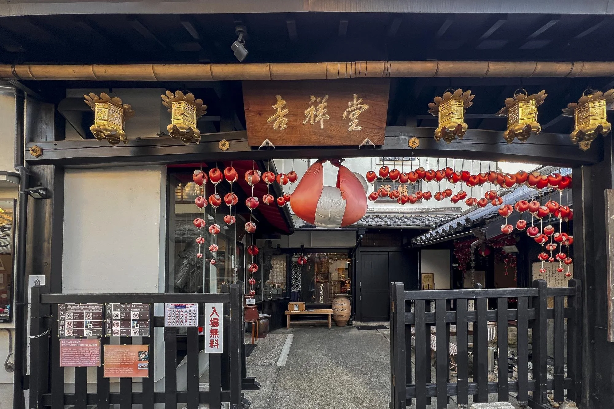 Traditional Japanese restaurant entrance decorated with red lanterns and a large paper lantern hanging in the center; wooden sign with Japanese characters above the entrance.