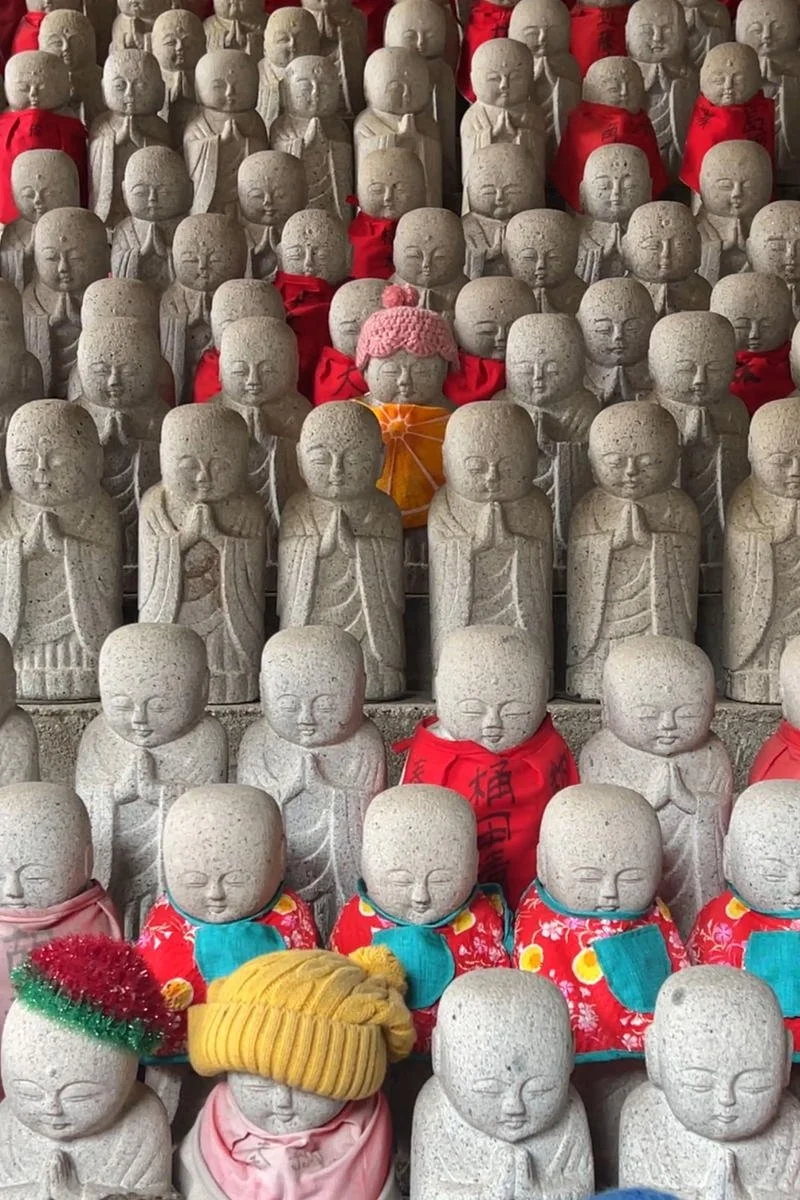 Multiple small Buddhist monk statues made of stone, some wearing colorful hats and red cloths, arranged in rows.