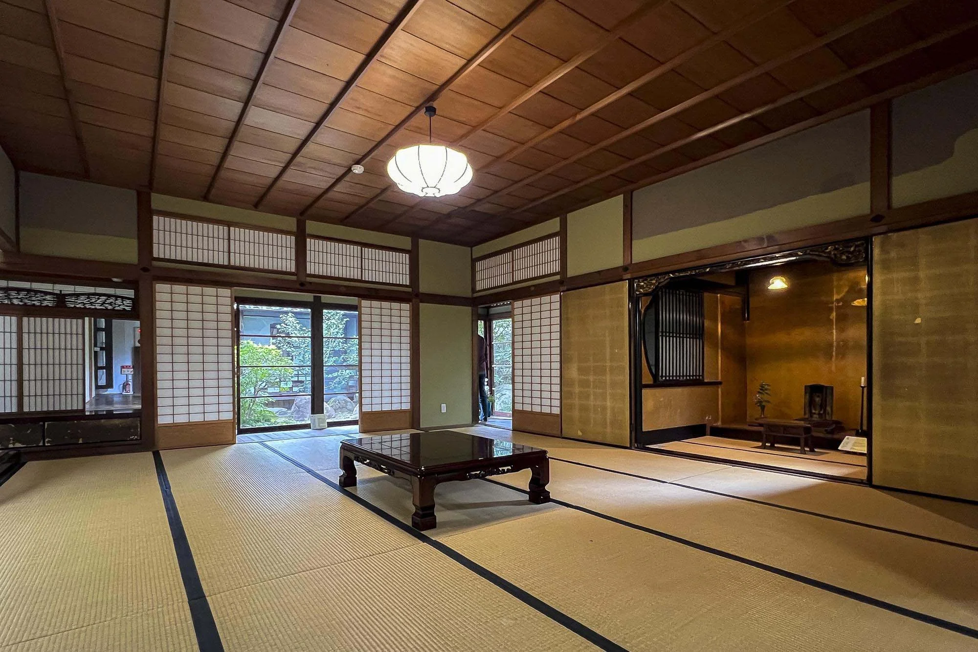 Traditional Japanese room with tatami mats, sliding shoji doors, a low wooden table, and a tokonoma alcove with a small display and plant.