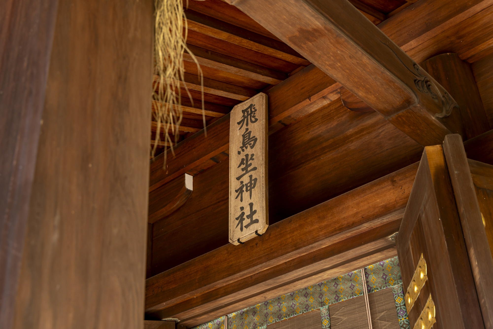 Wooden temple interior with a hanging wooden sign featuring Japanese characters.