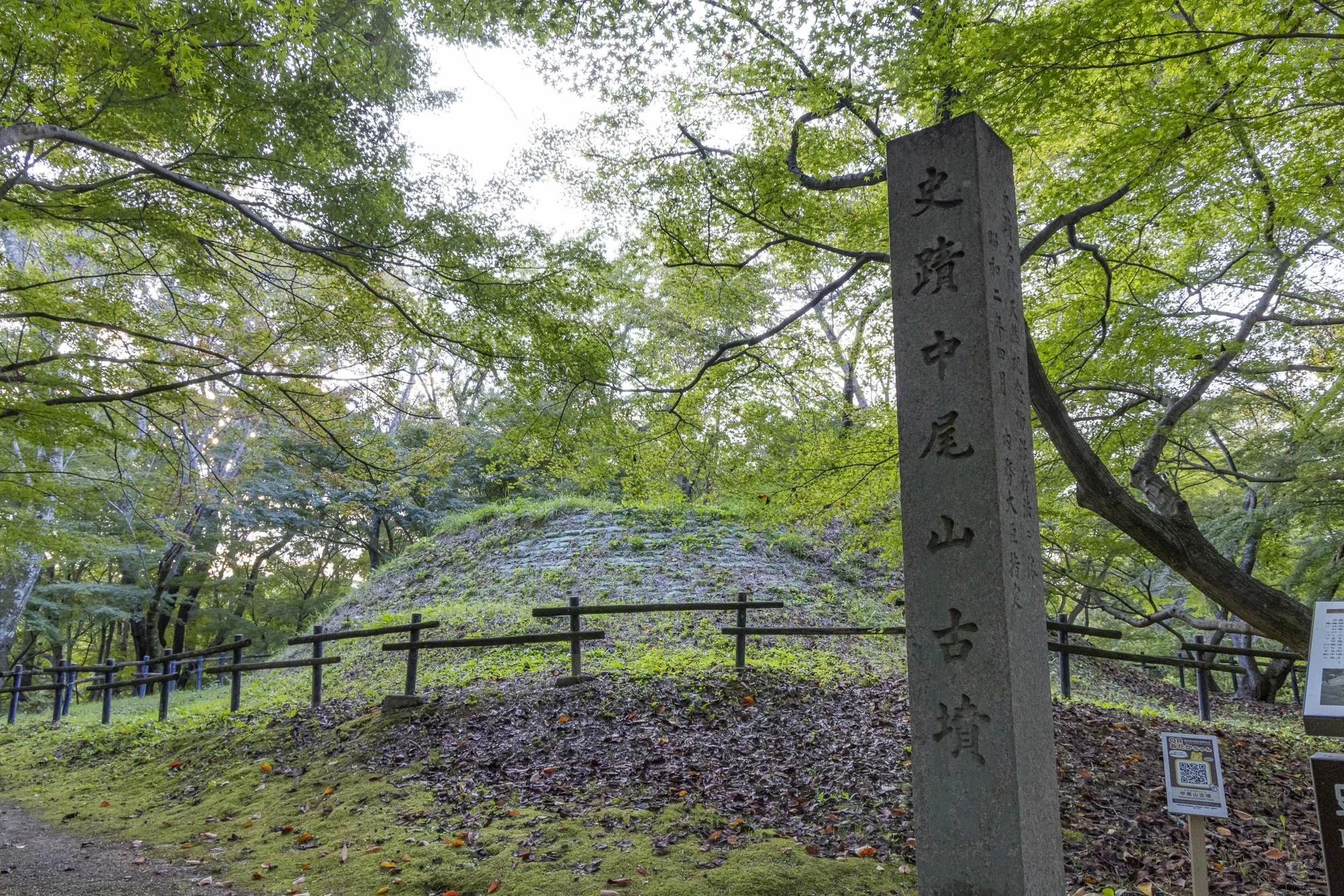 Nakaoyama Mounded Tomb: Ancient Japanese burial mound surrounded by green trees, with a stone monument inscribed in Japanese characters in the foreground.