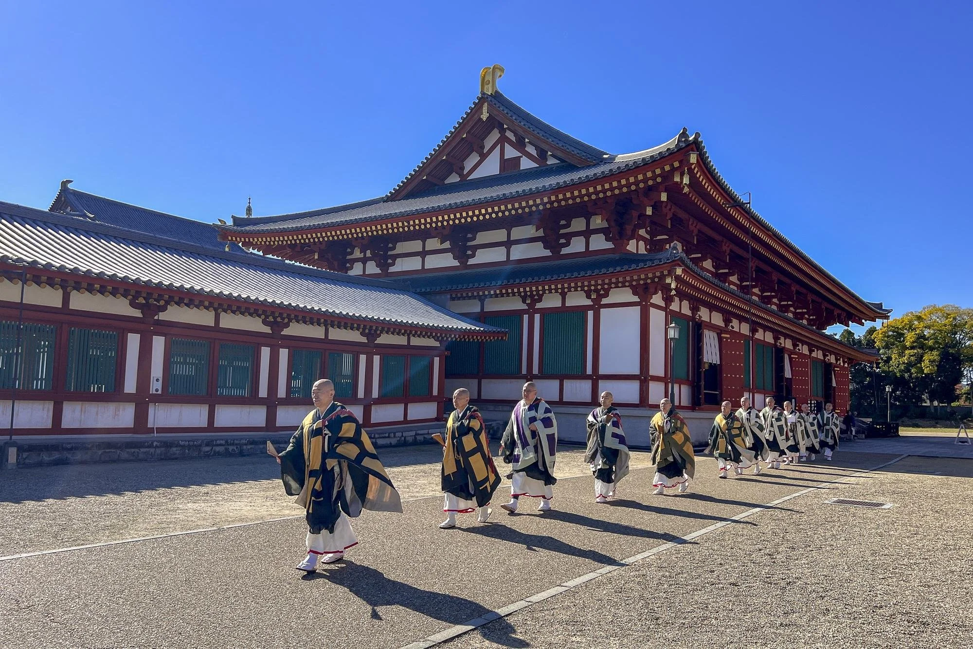 Yakushi-ji Temple: Monks walking in traditional robes outside a historic Japanese temple with a bright blue sky