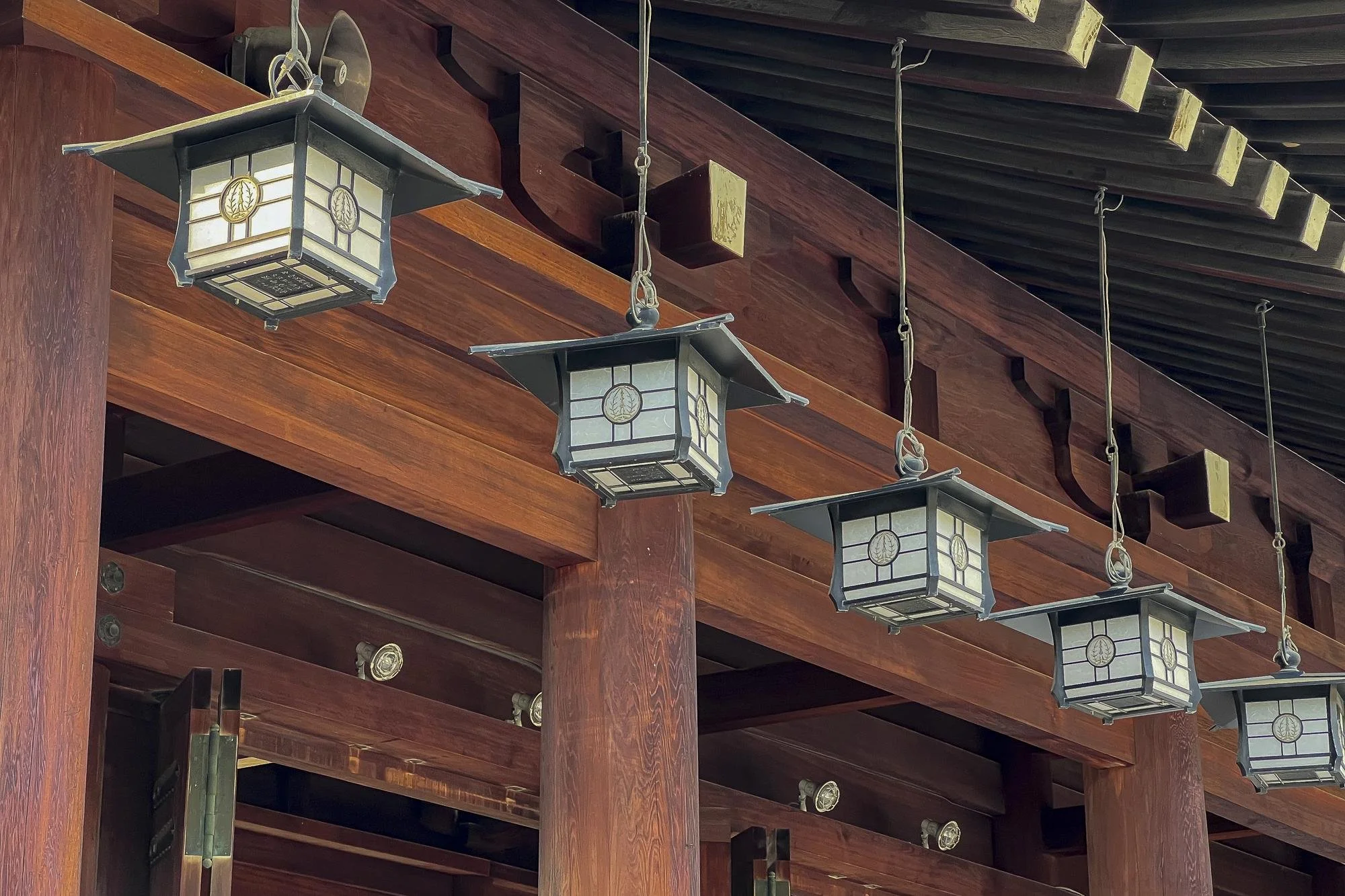 A row of traditional Japanese hanging lanterns with a pagoda-style roof, suspended from wooden beams in a temple or shrine setting.