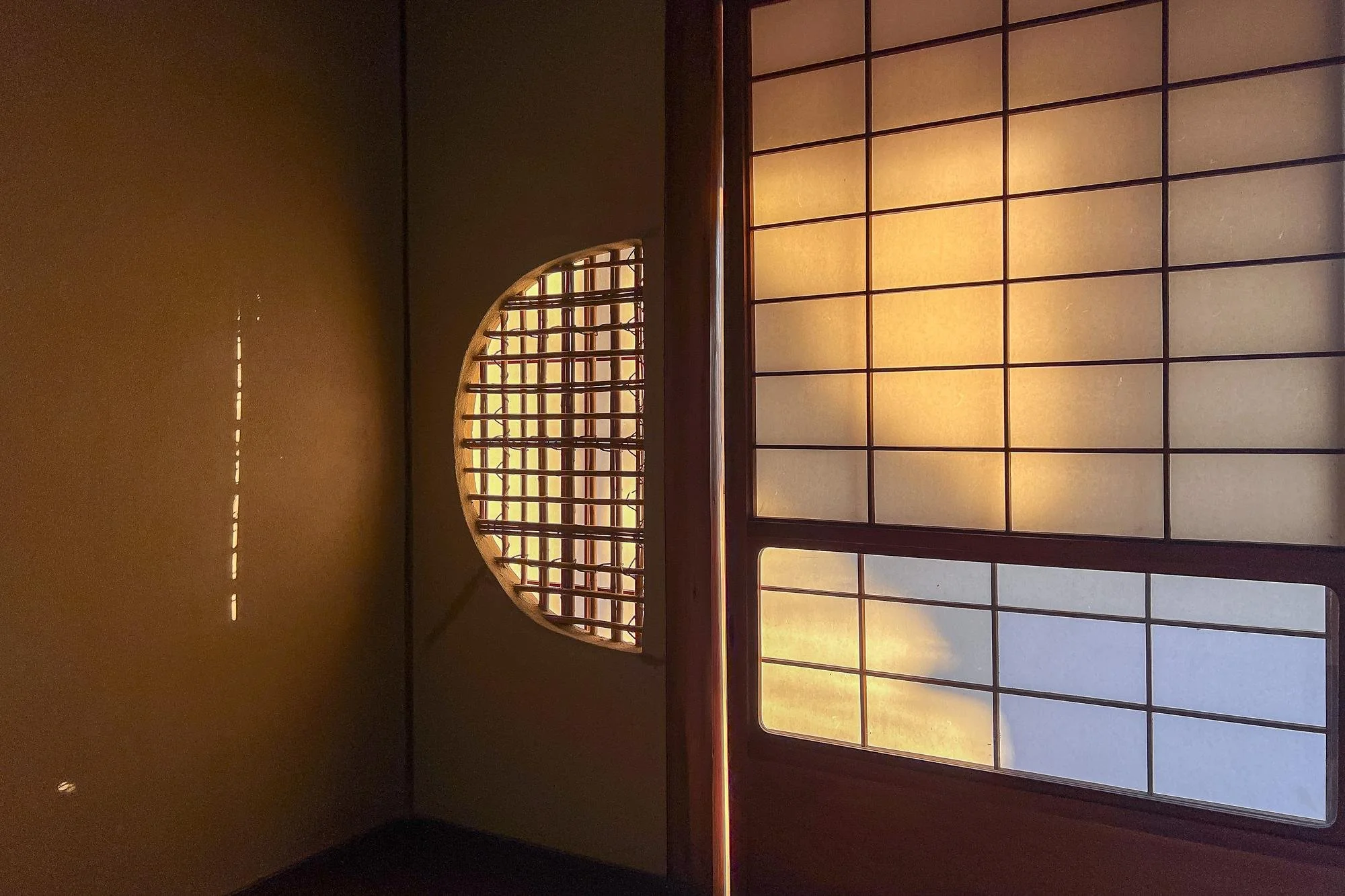 Interior of a traditional Japanese room with shoji sliding doors and a wooden lattice window, lit by warm natural light.