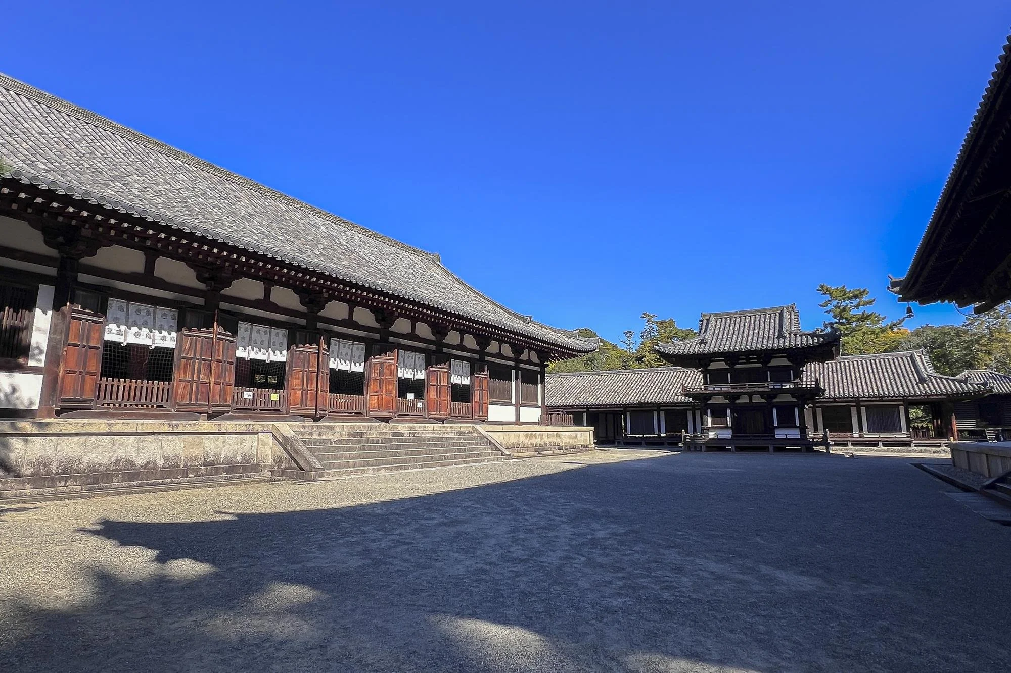 Traditional Japanese temple buildings with wooden floors, sliding doors, and tiled roofs under clear blue sky.
