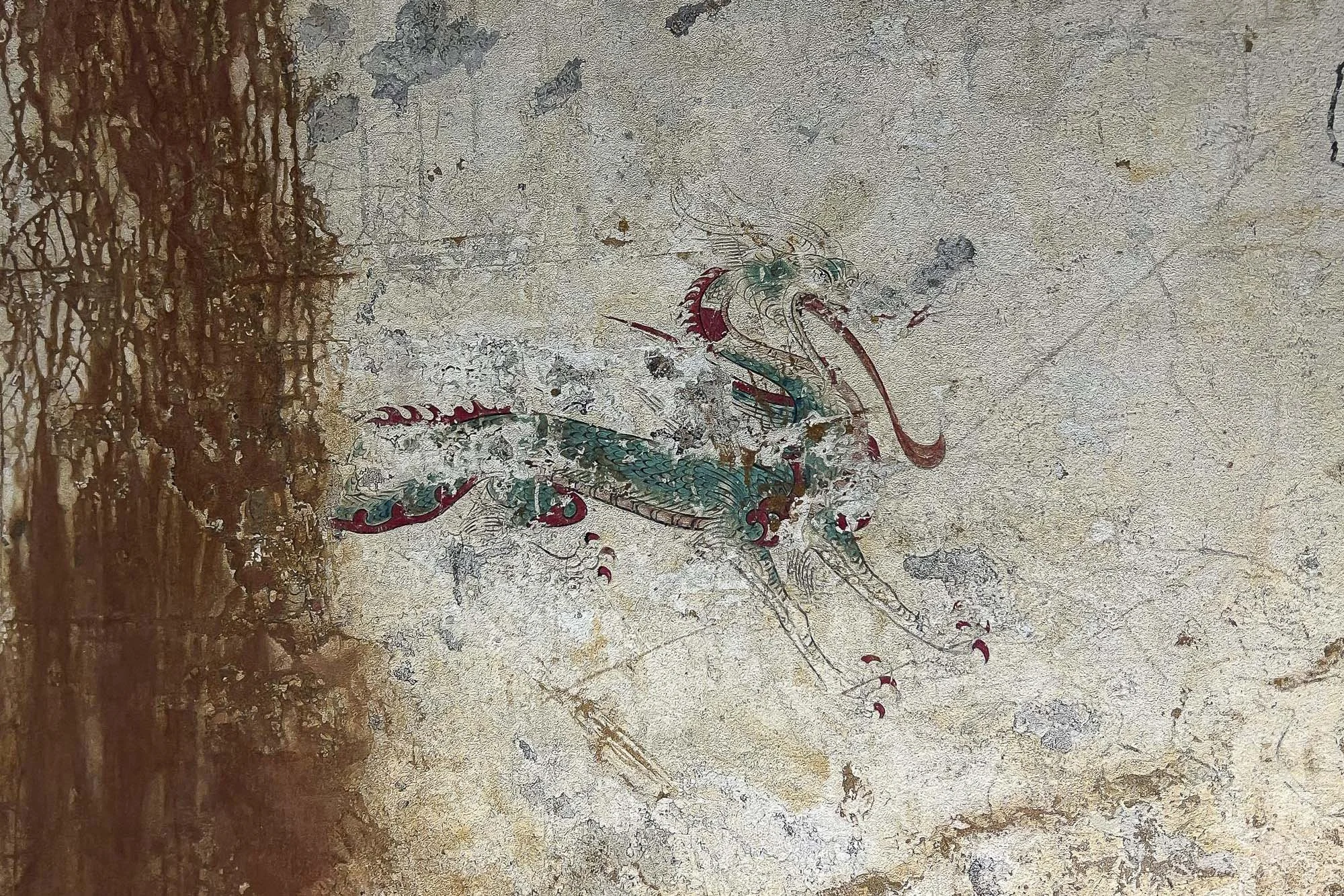 Ancient mural of a dragon painted on a weathered wall.