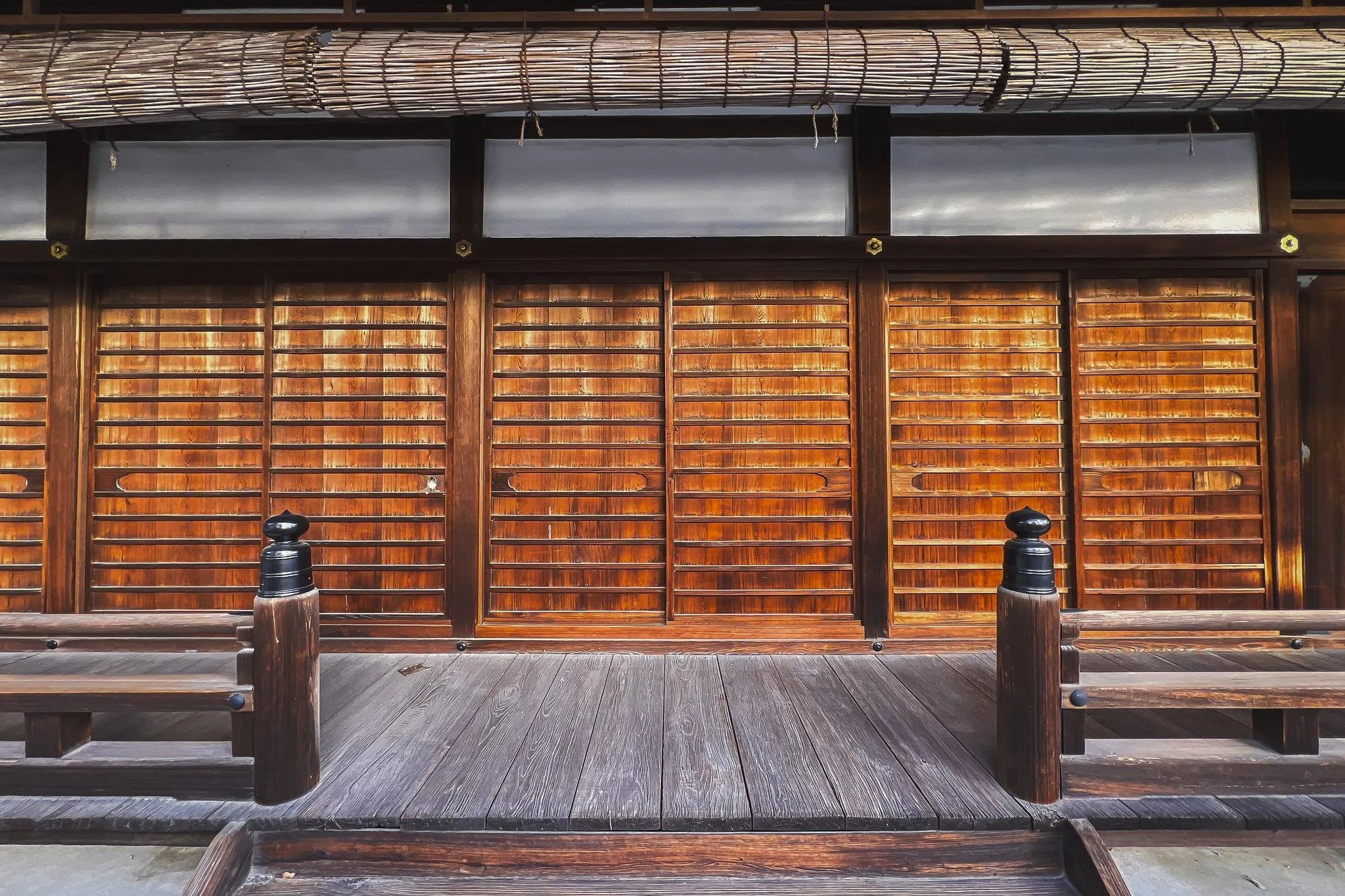 Wooden sliding doors with horizontal slats on a traditional Japanese building, flanked by two benches on a wooden porch.