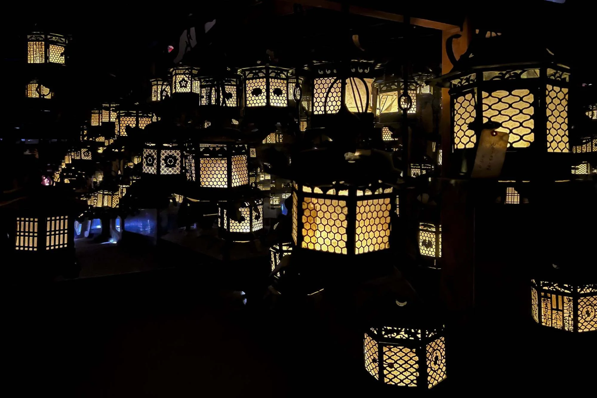 Multiple illuminated traditional Asian lanterns with geometric patterns hanging indoors, casting a warm glow.