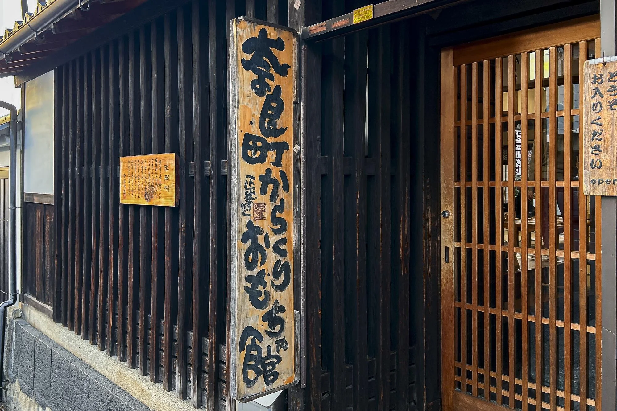 Japanese restaurant entrance with wooden vertical slats and two wooden signs with Japanese characters.