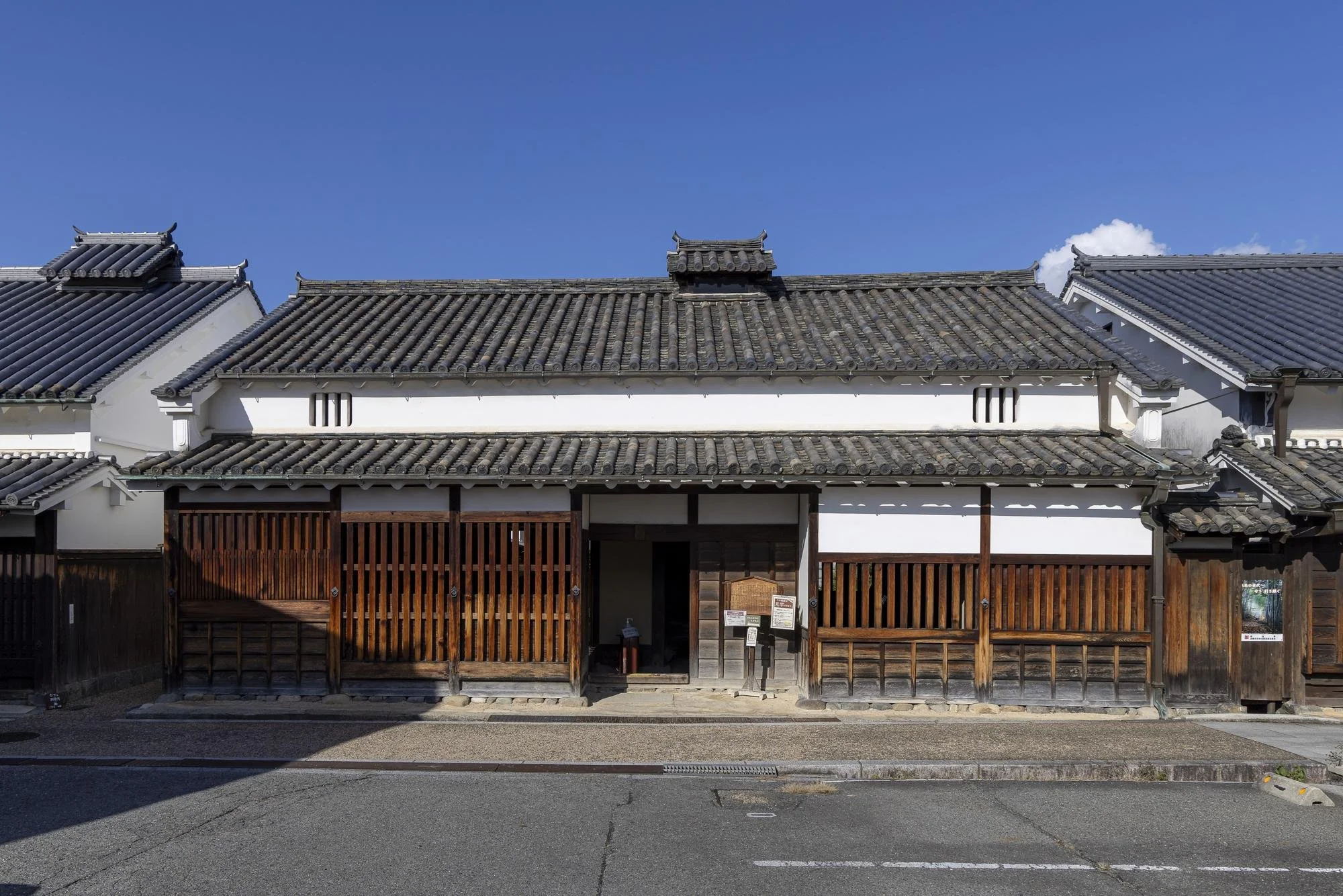 Traditional Japanese-style building with white walls, sliding wooden gates, and tiled roof under a blue sky.