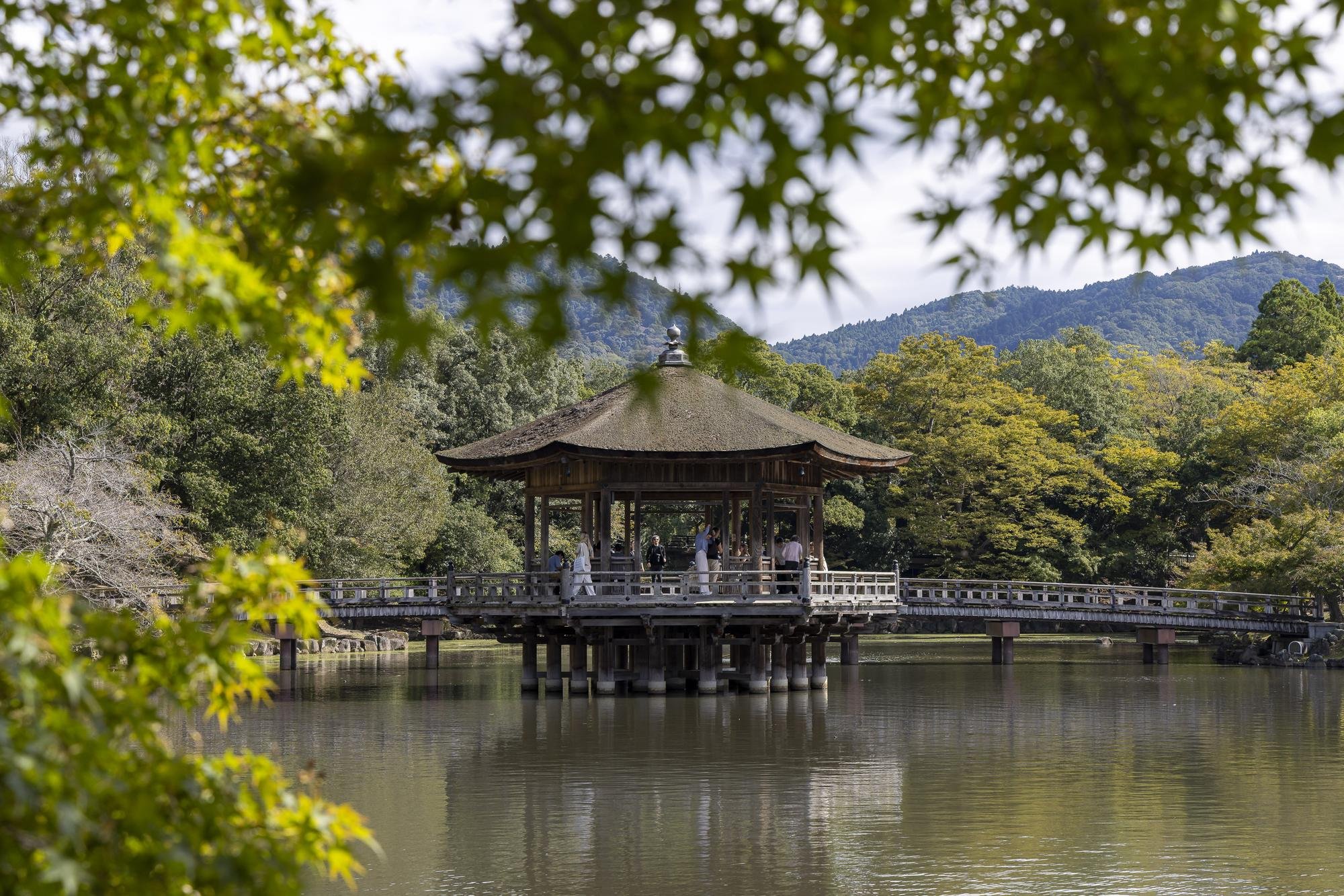 A traditional Japanese pavilion on a lake, surrounded by trees and mountains in the background.