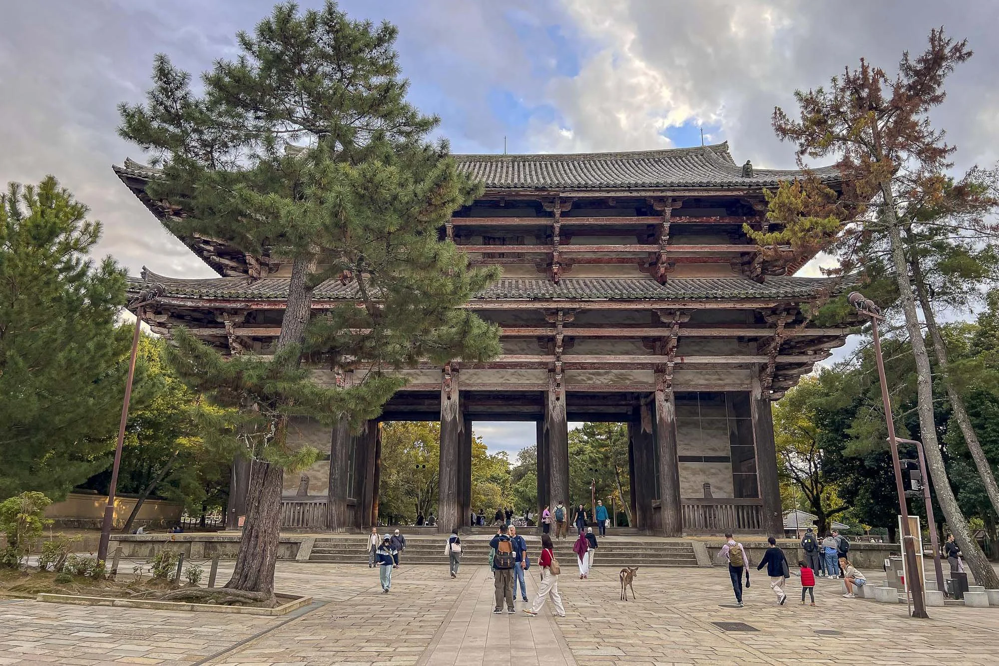 Traditional Japanese wooden temple gate with people walking and trees surrounding it.