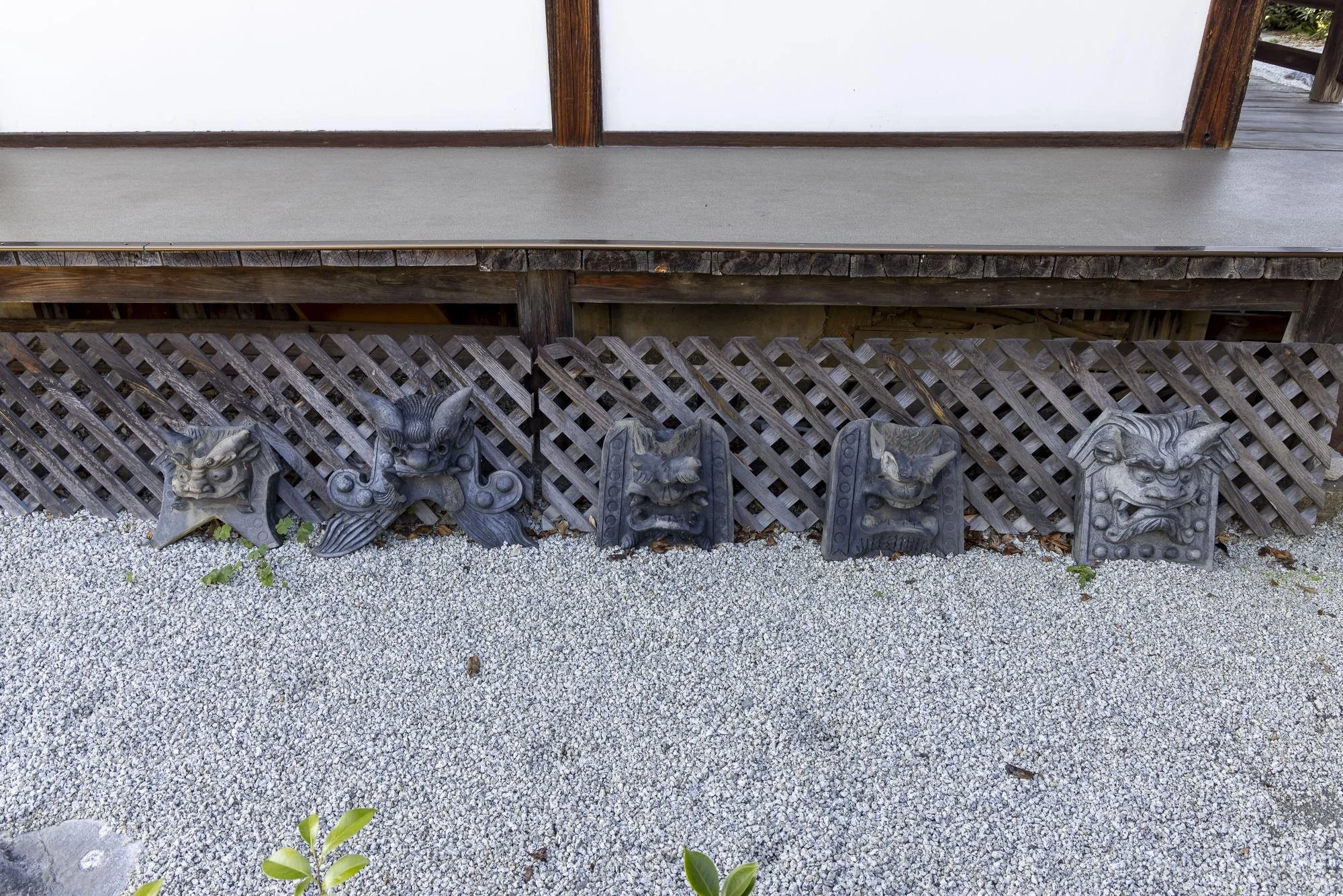 Five decorative Japanese ogre masks arranged on a lattice fence outside a building with a wooden deck and white walls.