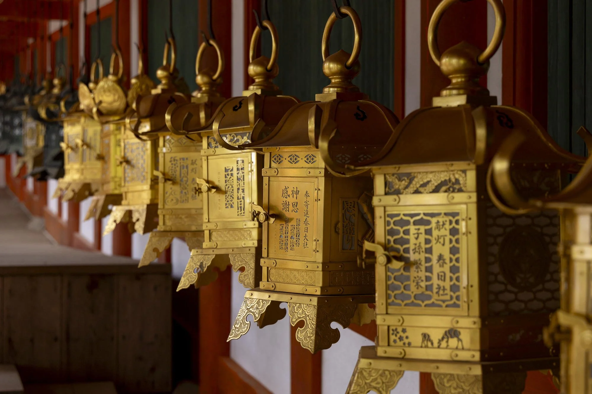 Row of ornate gold Japanese lanterns hanging along a temple wall.