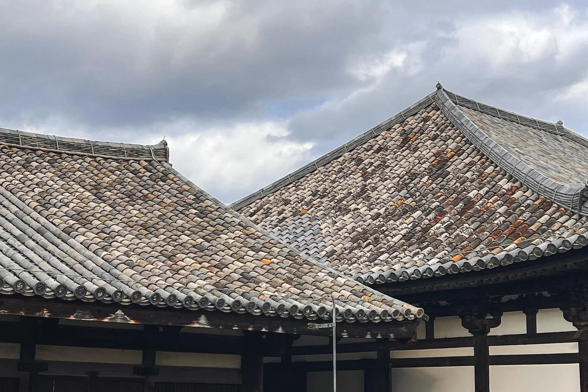 Traditional Japanese-style building with tiled sloped roofs and wooden support beams, under a cloudy sky.