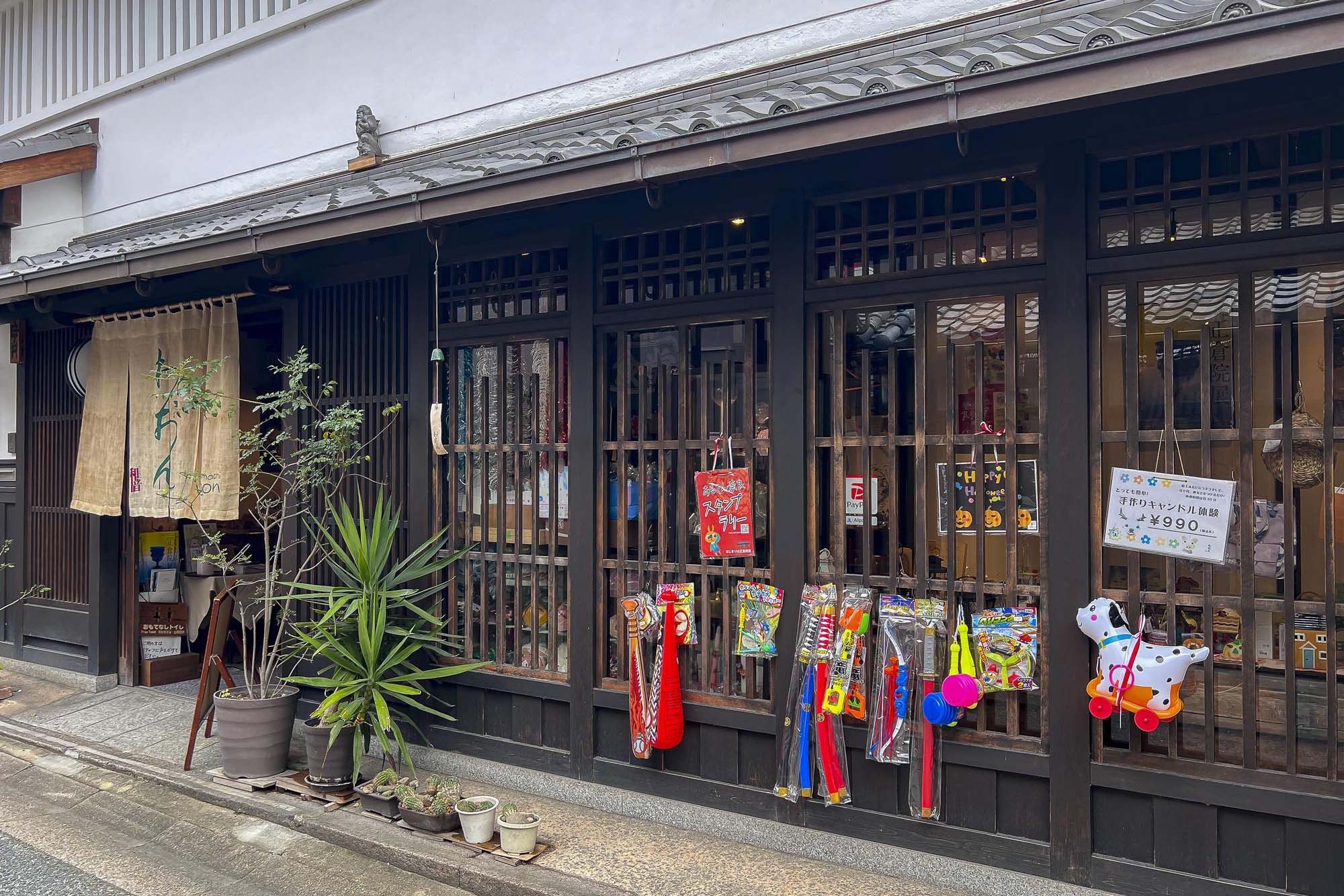 Traditional Japanese storefront with wooden lattice facade, decorated with colorful toys and a potted plant outside.