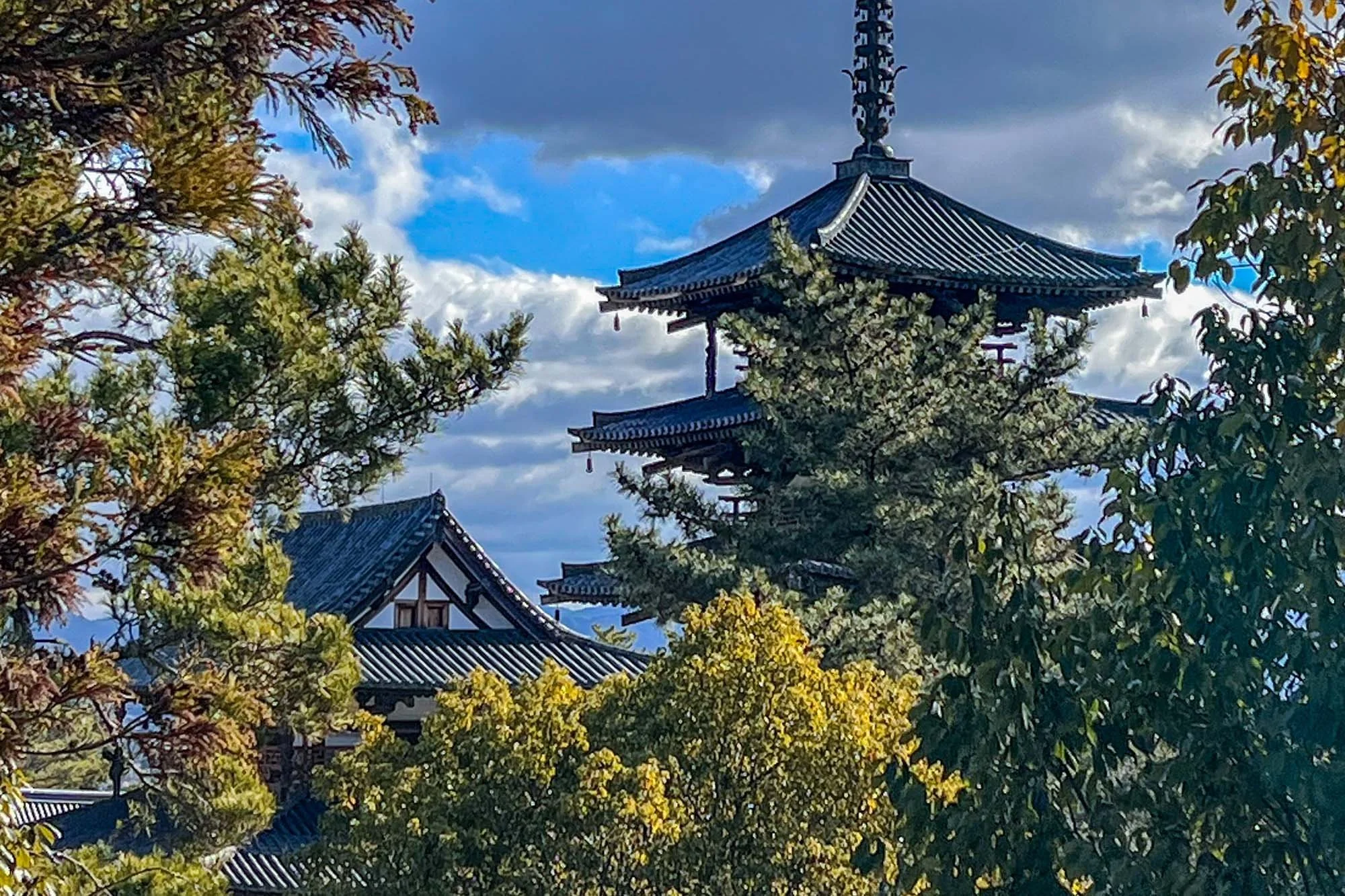 Horyu-ji Temple: Traditional Japanese pagoda surrounded by trees with green and yellow leaves, under a partly cloudy sky.
