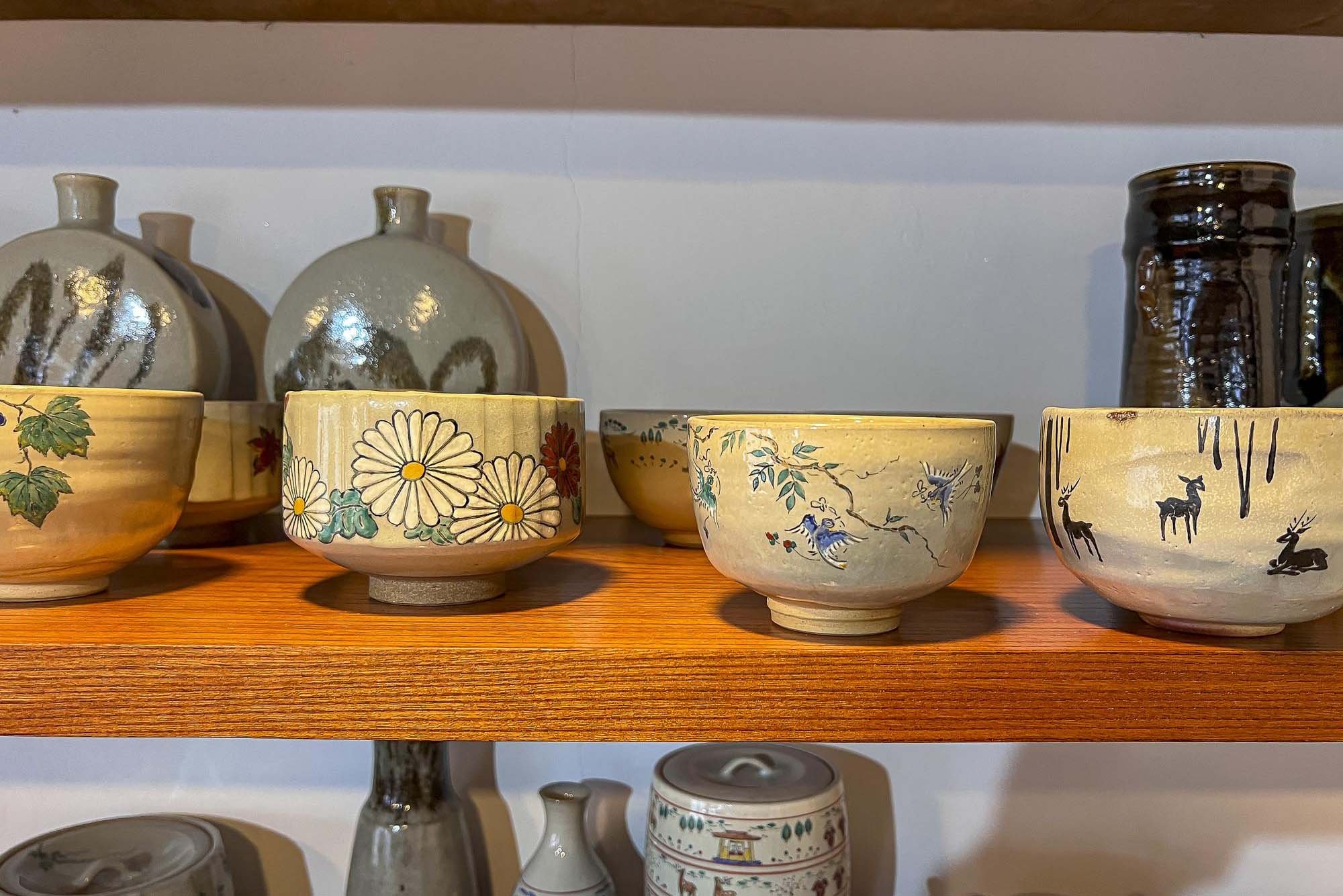 Decorative ceramic bowls with floral, bird, and animal designs displayed on a wooden shelf.