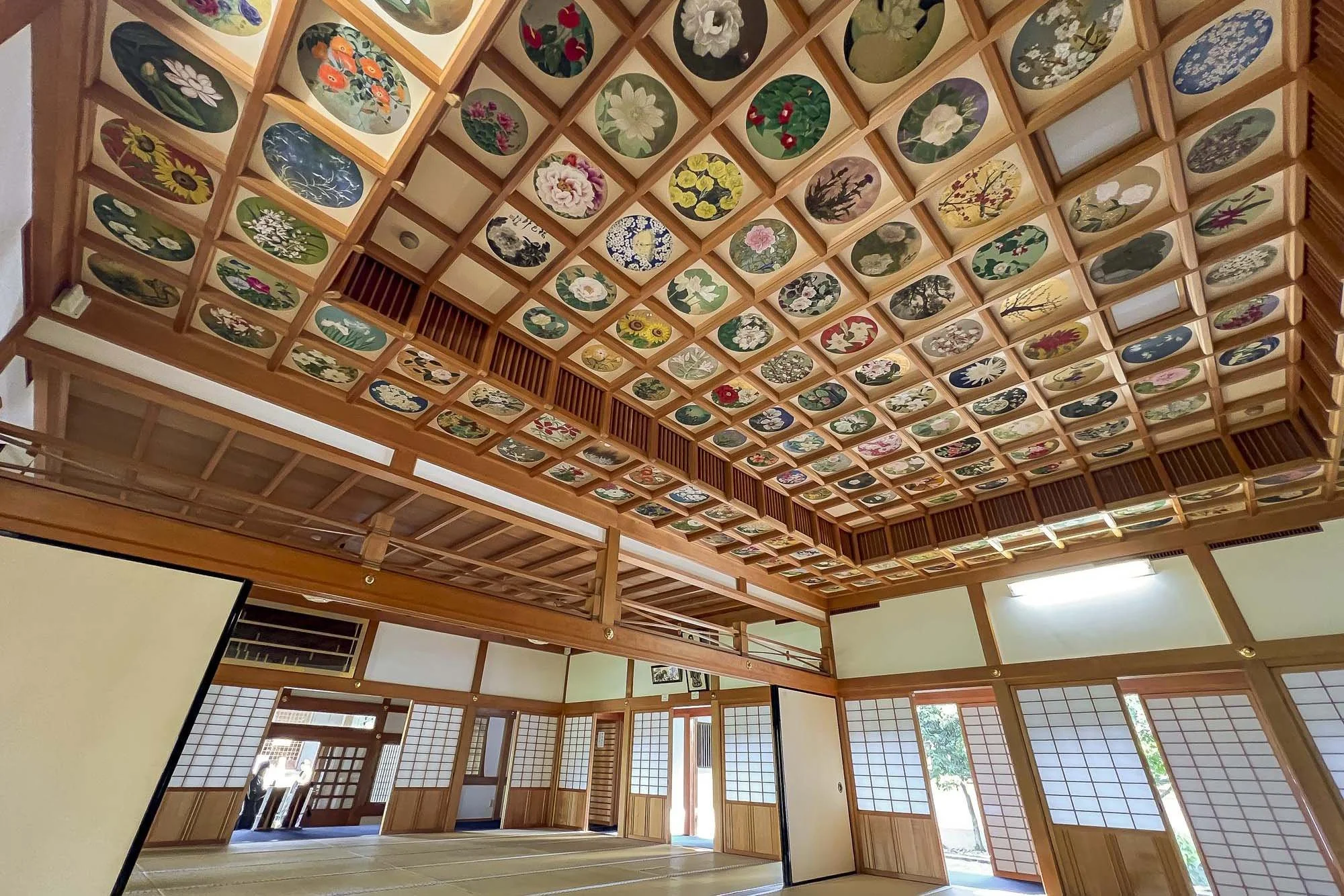 Traditional Japanese room interior with sliding shoji doors, tatami mats, and a ceiling decorated with artwork of various flowers and plants.