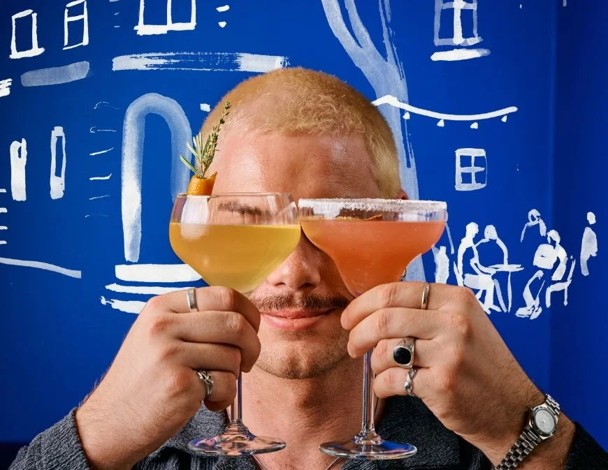 Two Neighbourhood Hour cocktails held up against Fern's hand-painted blue bar mural.