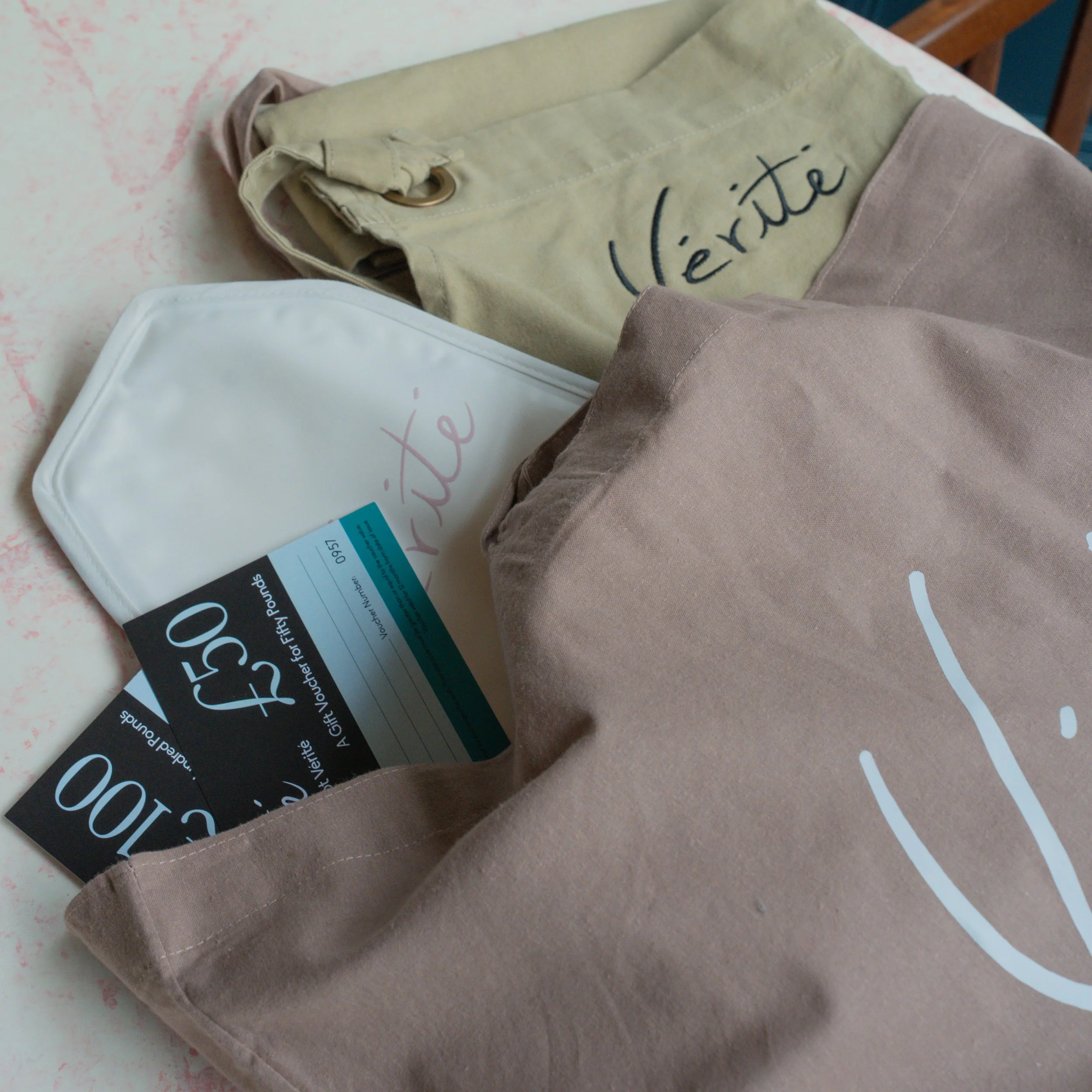 A beige tote bag and a white pouch on a light-colored surface, with two black tickets or passes partially visible inside the bag, all with the word 'vérité' written on them.