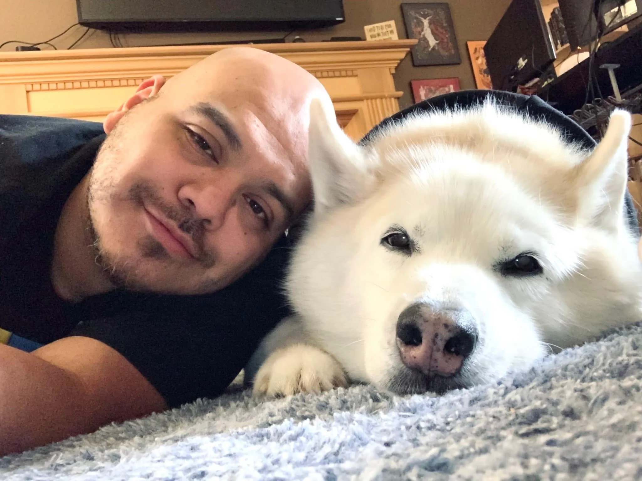 Ollie and his white husky, Dante, lying down together indoors.