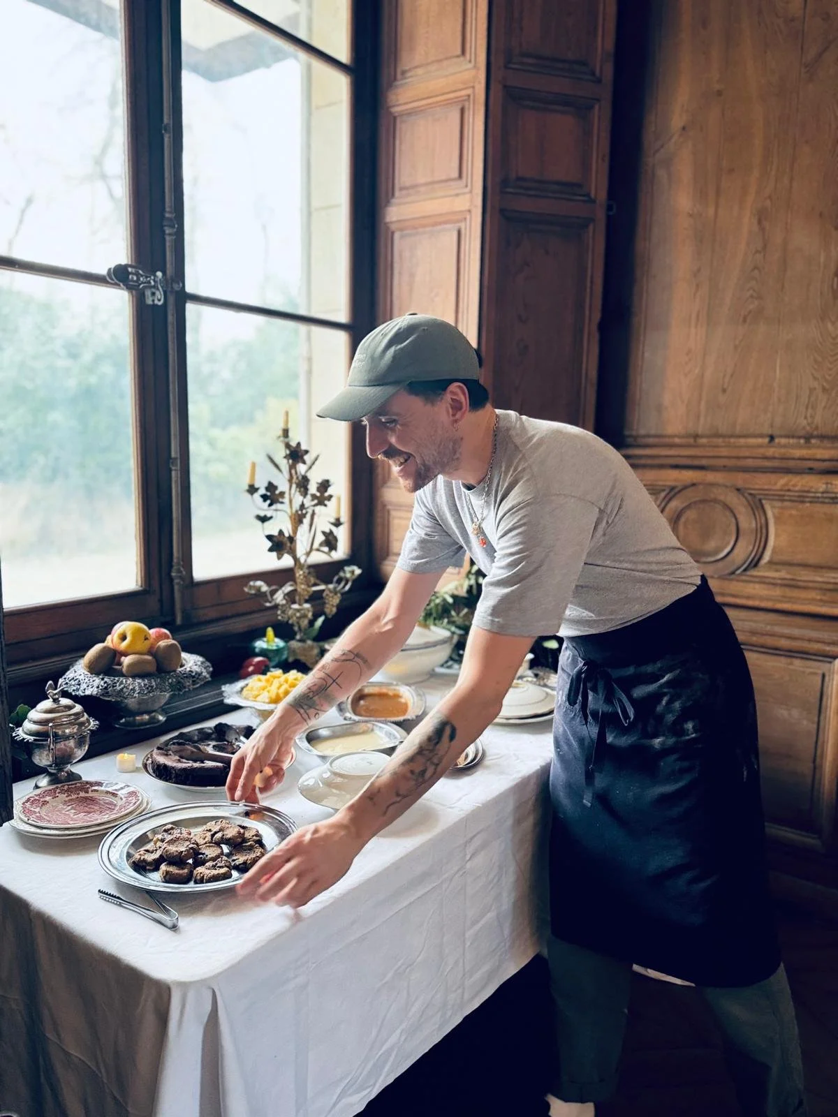 Un homme sert des biscuits sur une table de petit-déjeuner dans une pièce en bois, près d'une grande fenêtre.