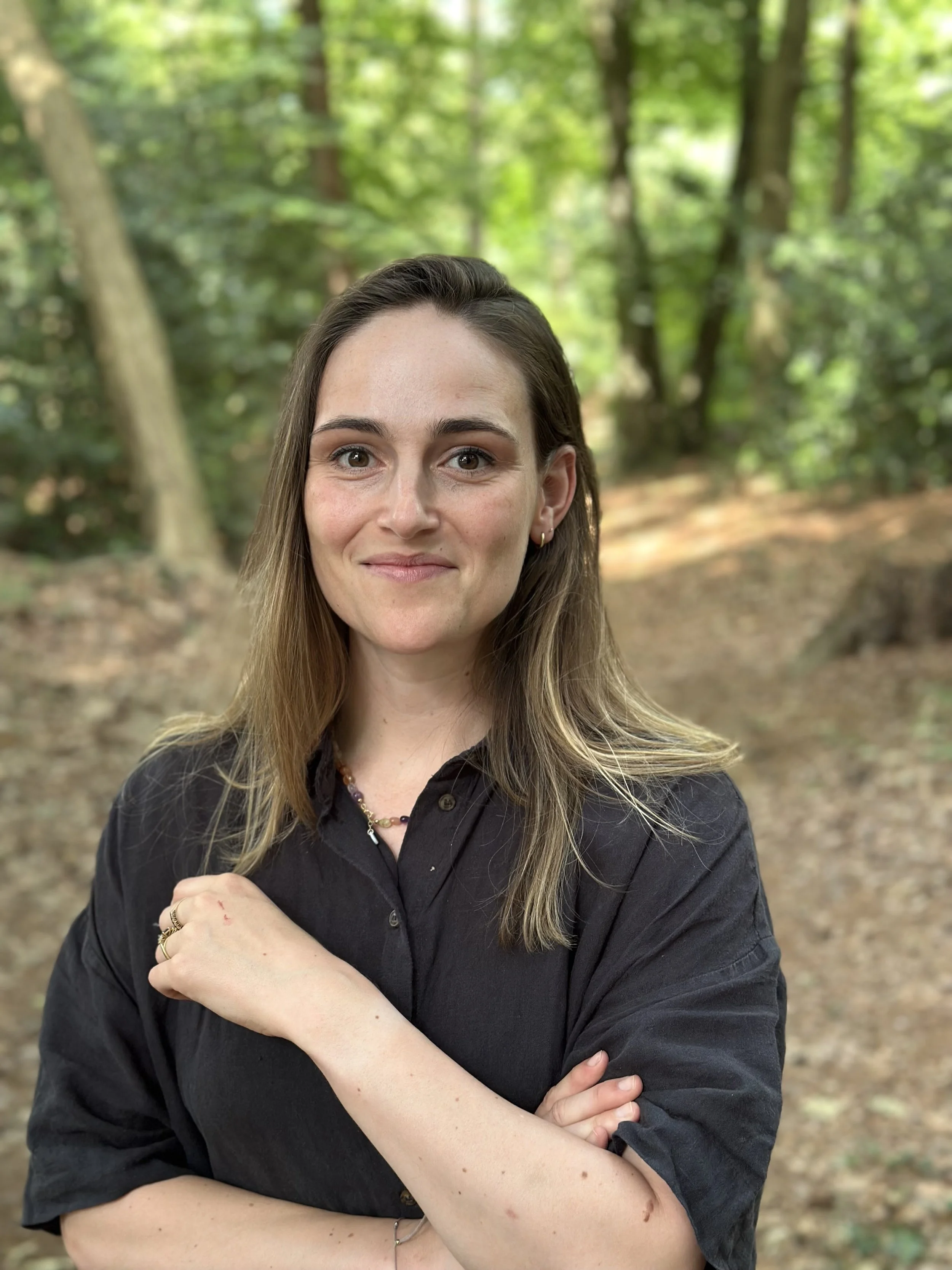 Portret van een jonge vrouw met lang haar, in een bos, glimlachend en gekleed in een zwart shirt.