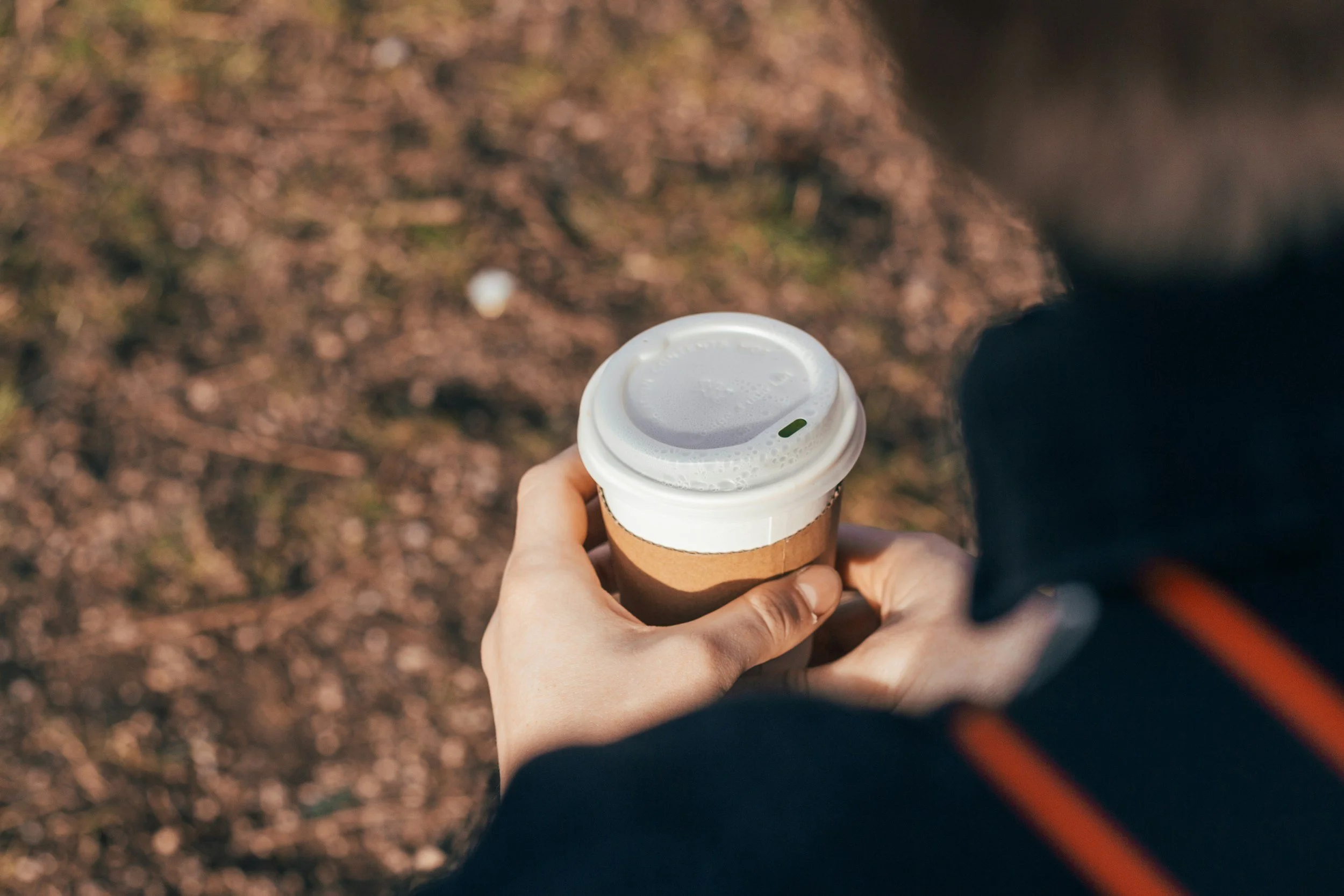 Person holding a disposable coffee cup outdoors on a warm, sunny day.