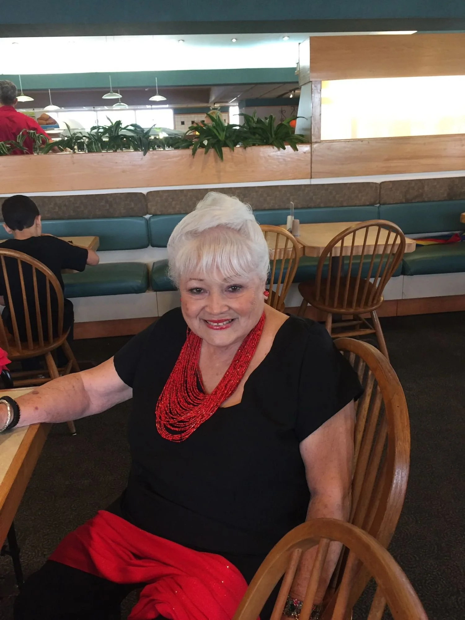 Madre de Yeida Cruz sonriendo mientras disfruta un encuentro social en un restaurante, representando bienestar emocional, socialización y acompañamiento comunitario en la adultez mayor.