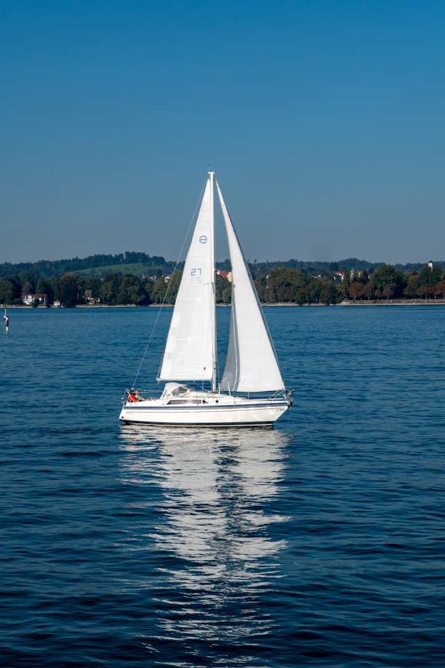 A white sailing boat on water on a bright day with green hills and trees in the background