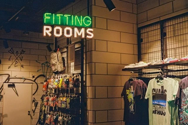 Inside a clothing store with a neon sign that says fitting rooms