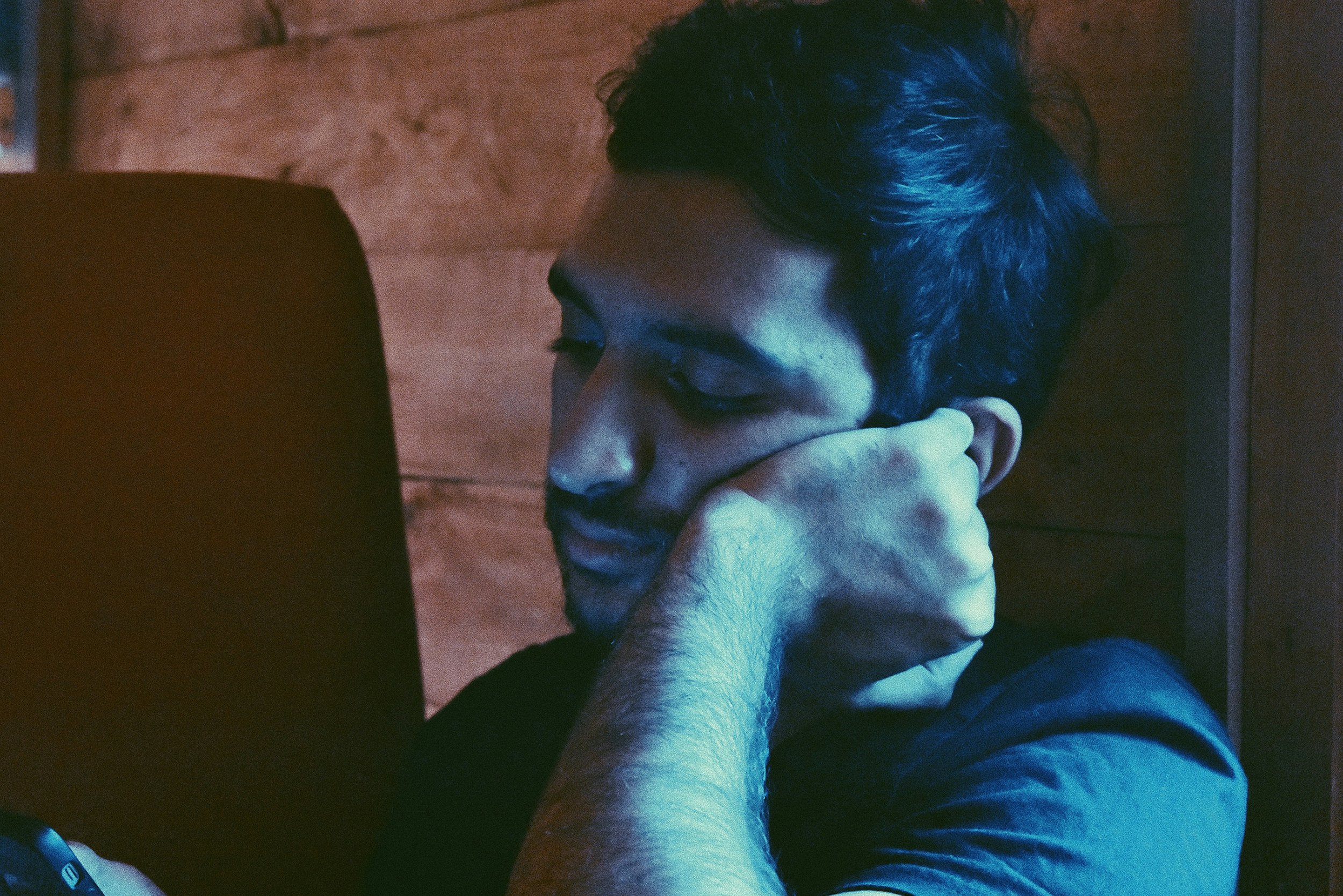 Person leaning on their hand looking contemplative while engaging with a device, illustrating using dating apps during boredom or emotional regulation.