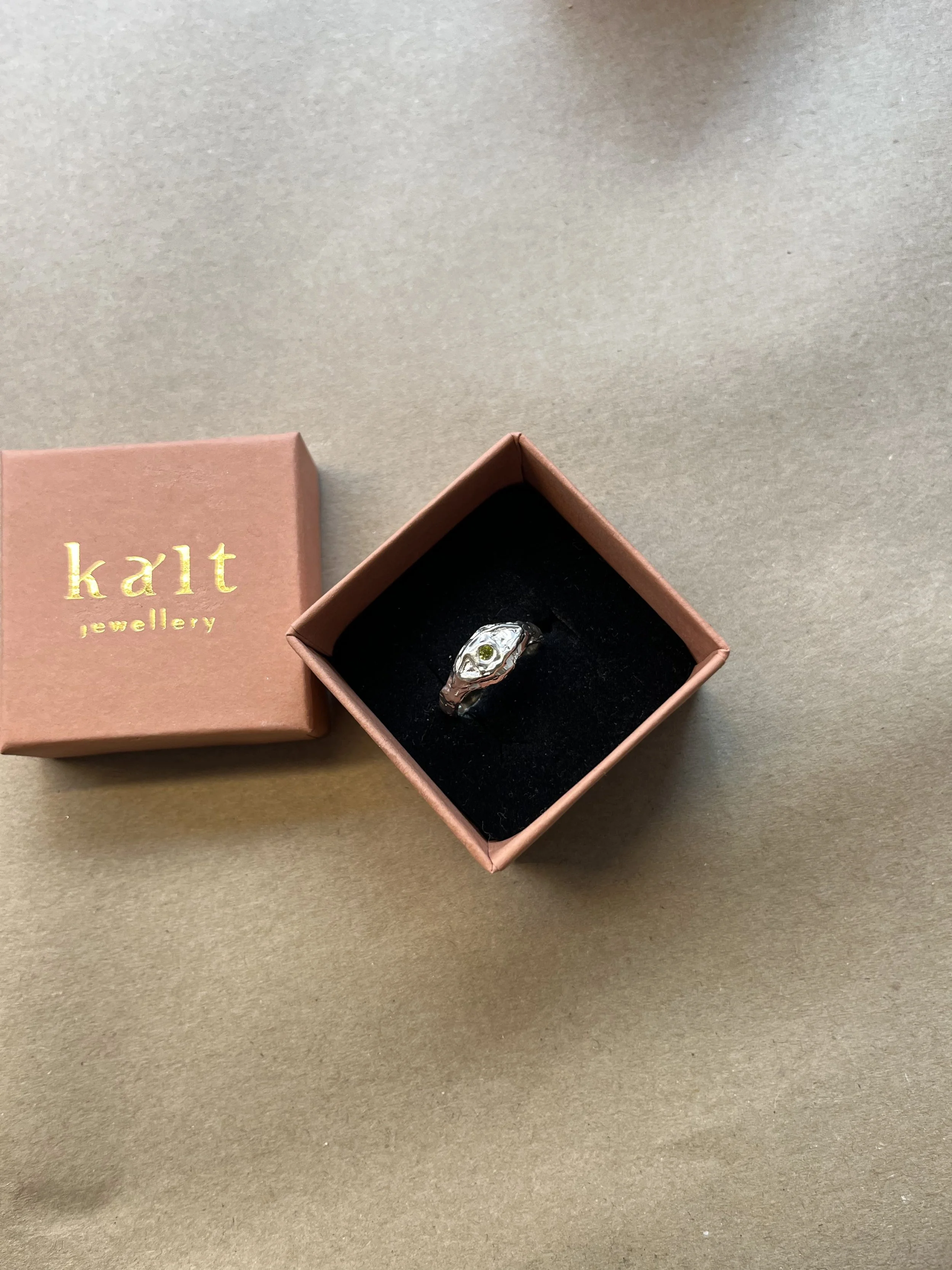 A silver ring with a textured, uneven surface on a white, brushed wooden surface.