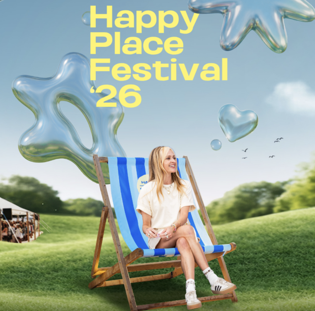 A young woman sitting on a blue and white striped deck chair outdoors at the Happy Place Festival 2026. The background features green grass, trees, and floating colorful star and heart-shaped balloons in the sky, with a tent visible on the left.