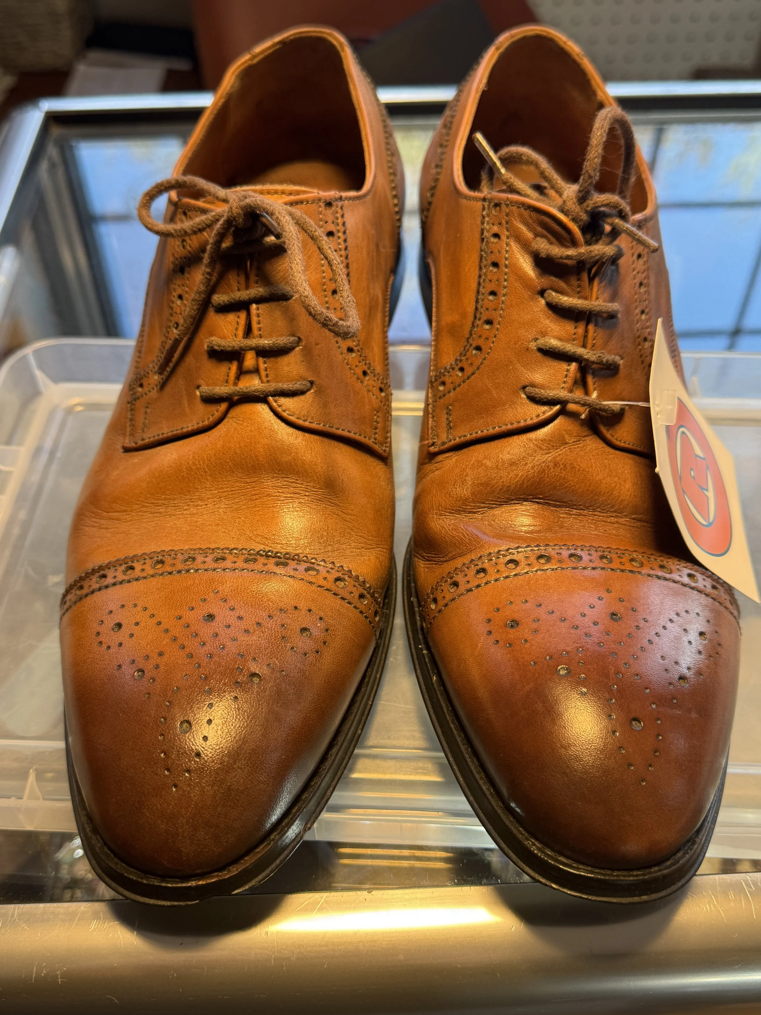 Pair of vintage brown leather dress shoes with decorative perforations, laced and displayed on a clear plastic container.