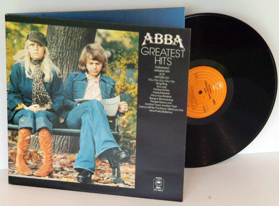 Vinyl record of ABBA's Greatest Hits album with cover art showing two people sitting on a park bench during autumn.
