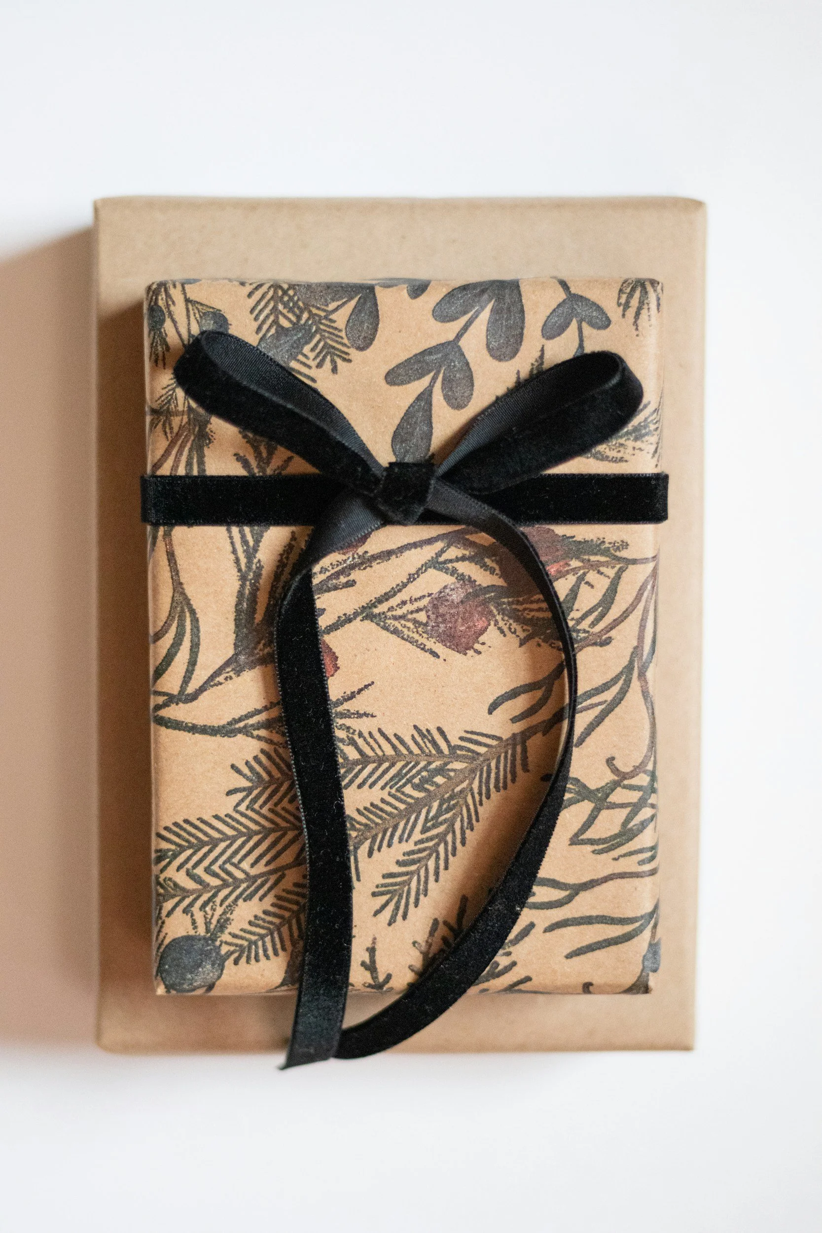 A gift box wrapped in brown paper with black botanical illustrations, tied with a black ribbon