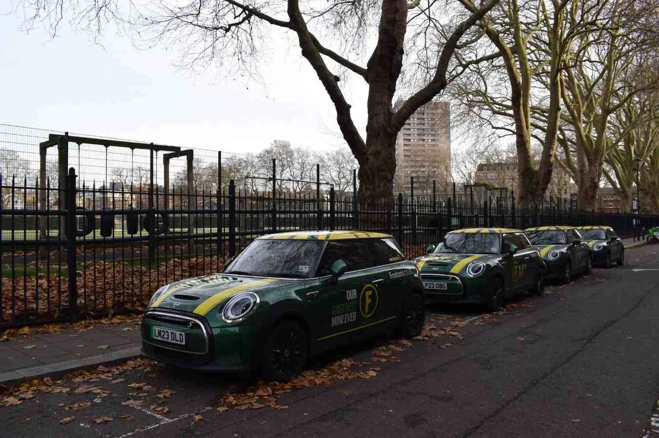 A row of green and yellow branded electric MINI Cooper cars parked on a London street, representing a company EV fleet.