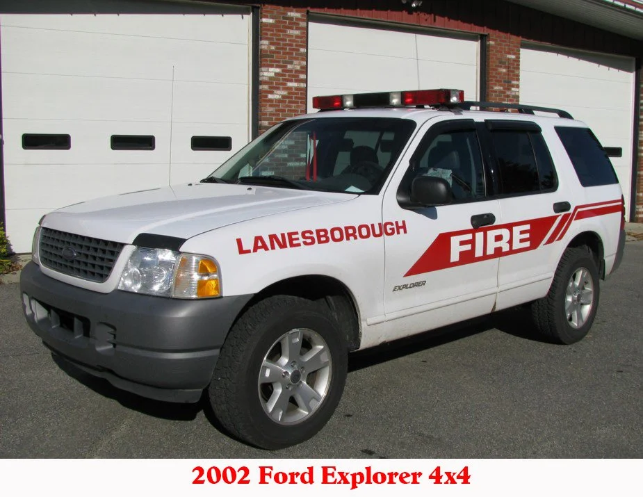 White 2002 Ford Explorer 4x4 with Lanesborough Fire Department markings and emergency lights, parked in front of a brick building with white garage doors.